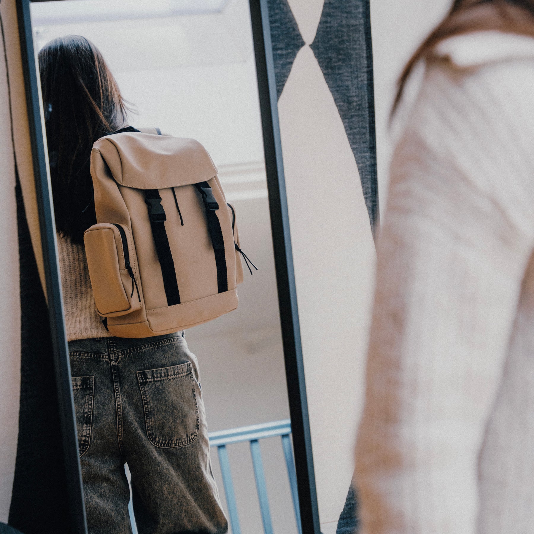 Person trägt den beigen Rucksack 'Finley' mit schwarzen Riemen und seitlichen Taschen, gesehen im Spiegel