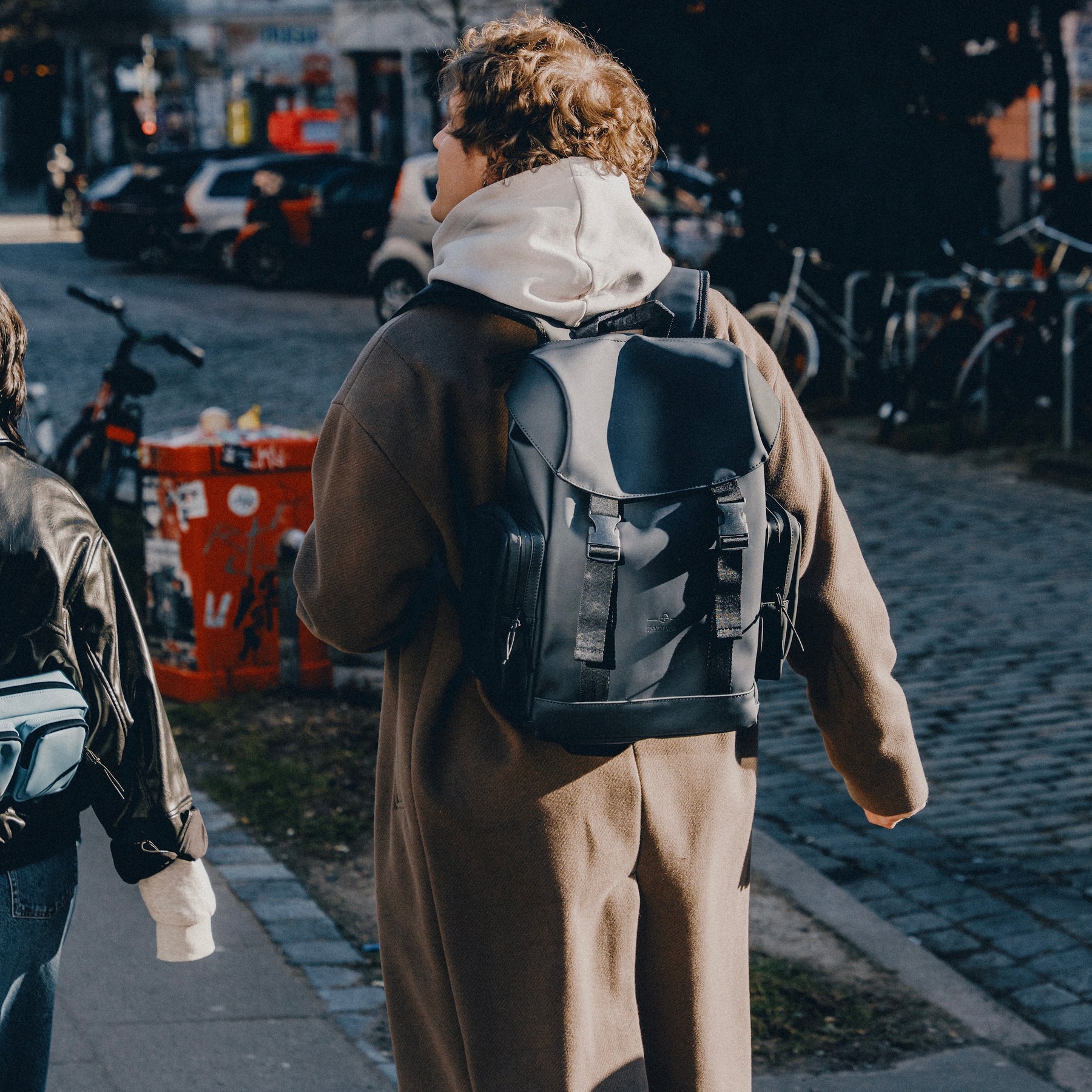 Person trägt braunen Mantel und schwarzen Rucksack 'Finley' beim Gehen in der Stadt