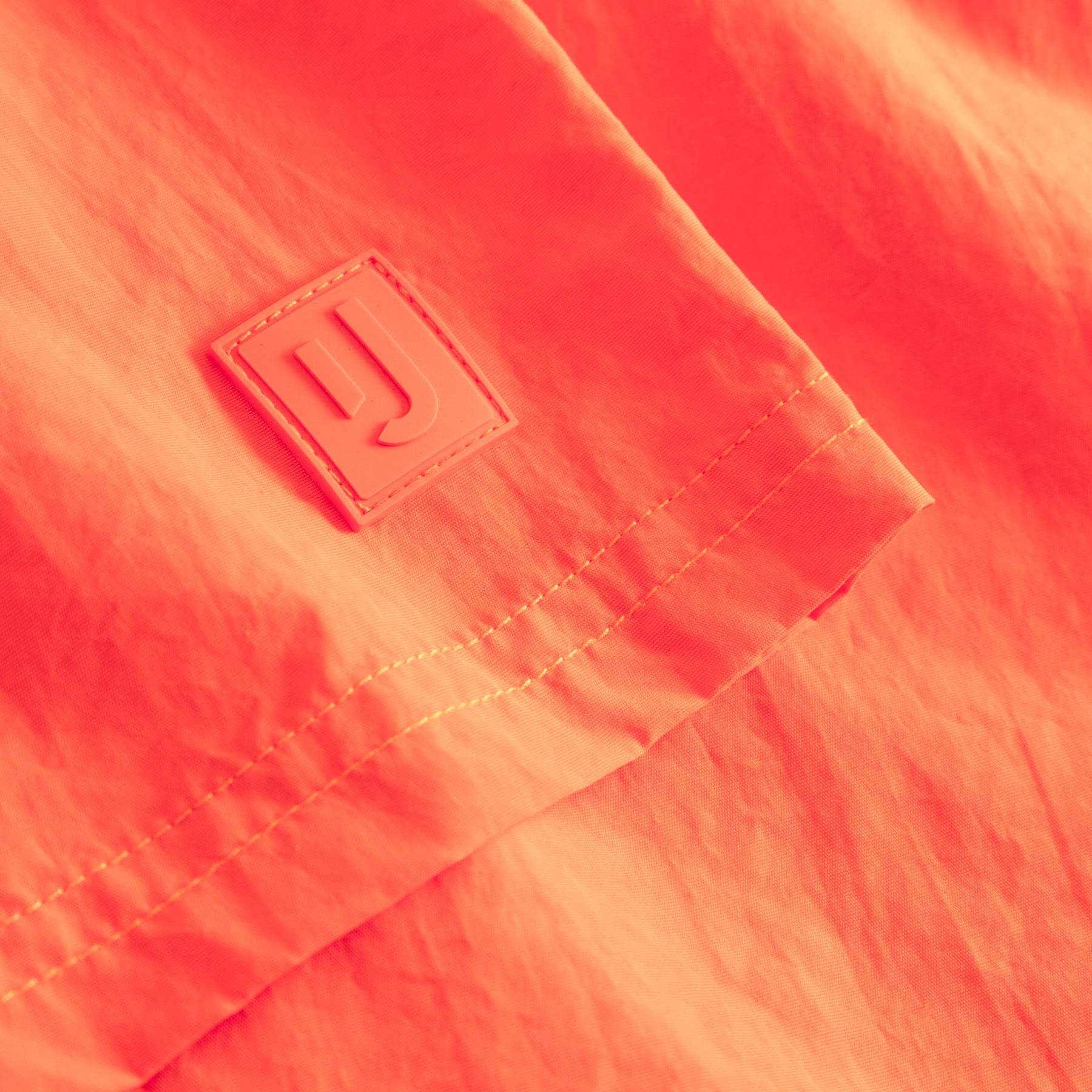 Nahaufnahme der orangen Badehose 'Jay' mit Johnny Urban Logo auf einem kleinen Aufnäher