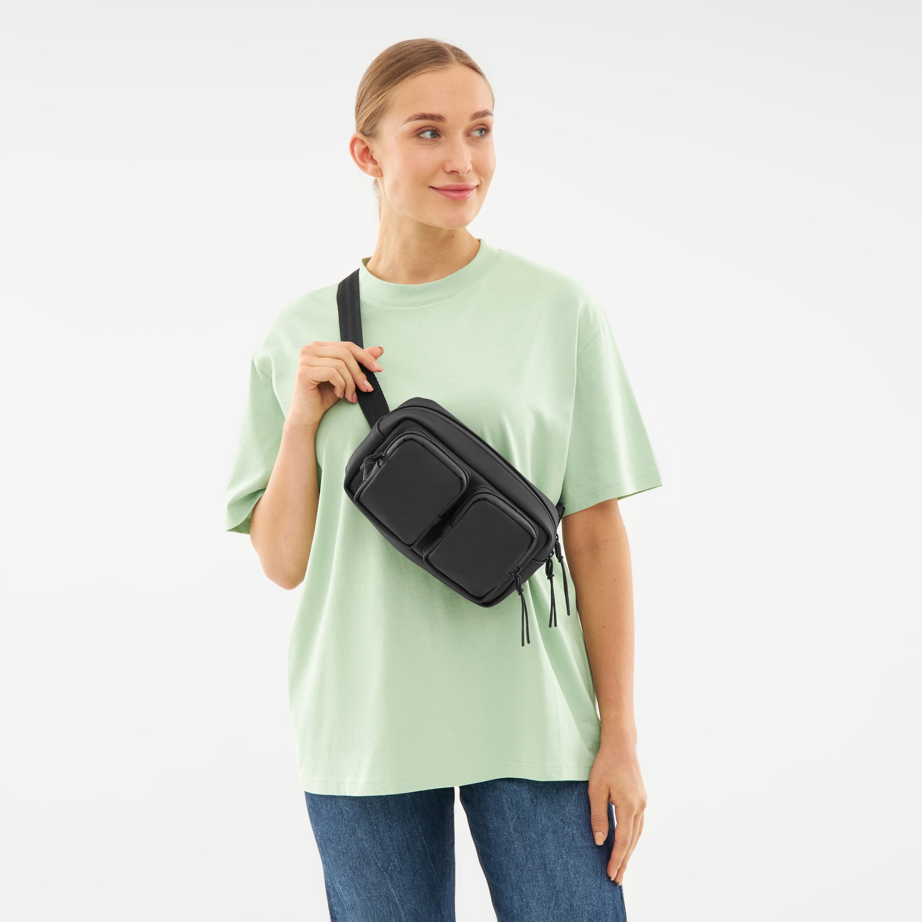 Frau trägt schwarze Umhängetasche 'Wesley' mit zwei vorderen Taschen über mintgrünem T-Shirt und Jeans