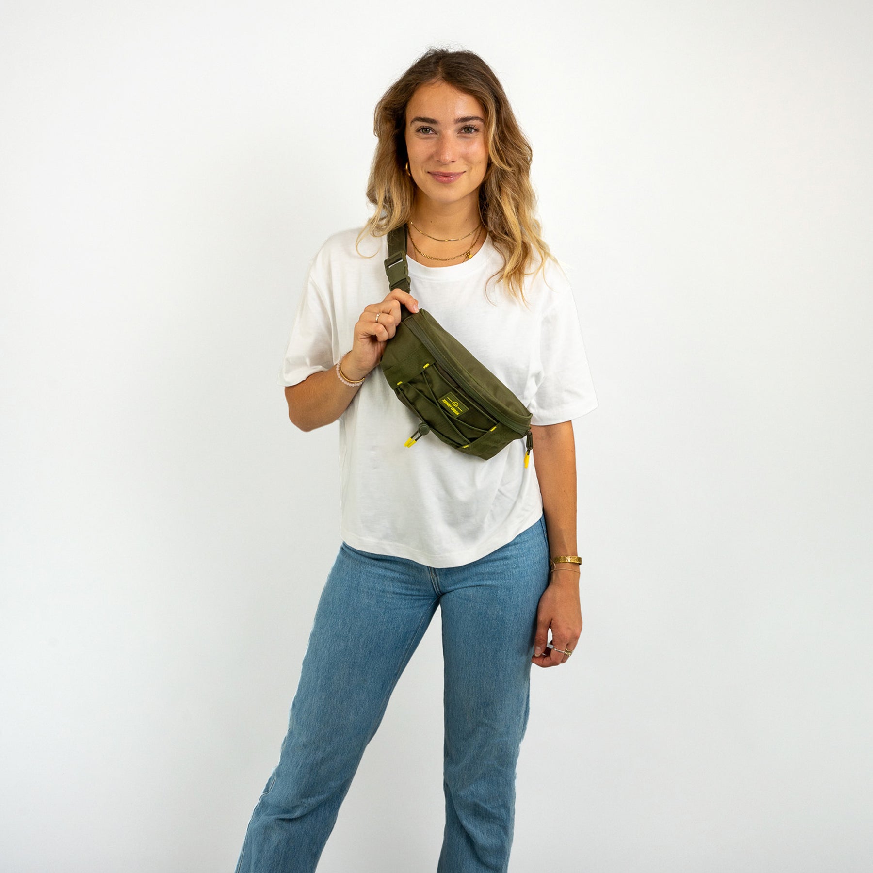 Frau trägt olivgrüne Bauchtasche 'Devin' von Johnny Urban über der Schulter zu weißem T-Shirt und blauen Jeans