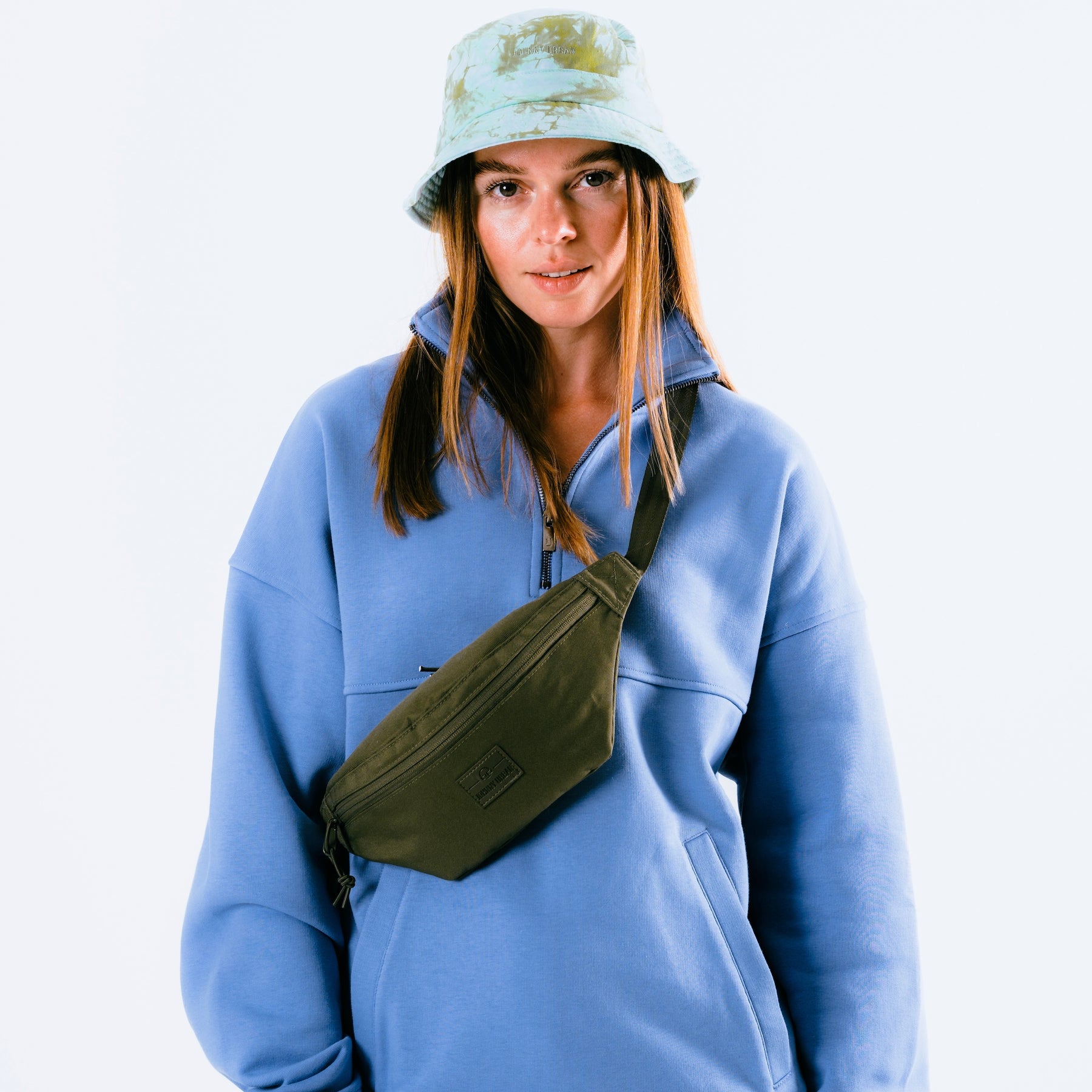 Frau trägt olivgrüne Johnny Urban Bauchtasche 'Erik Small' über blauem Pullover mit Reißverschluss