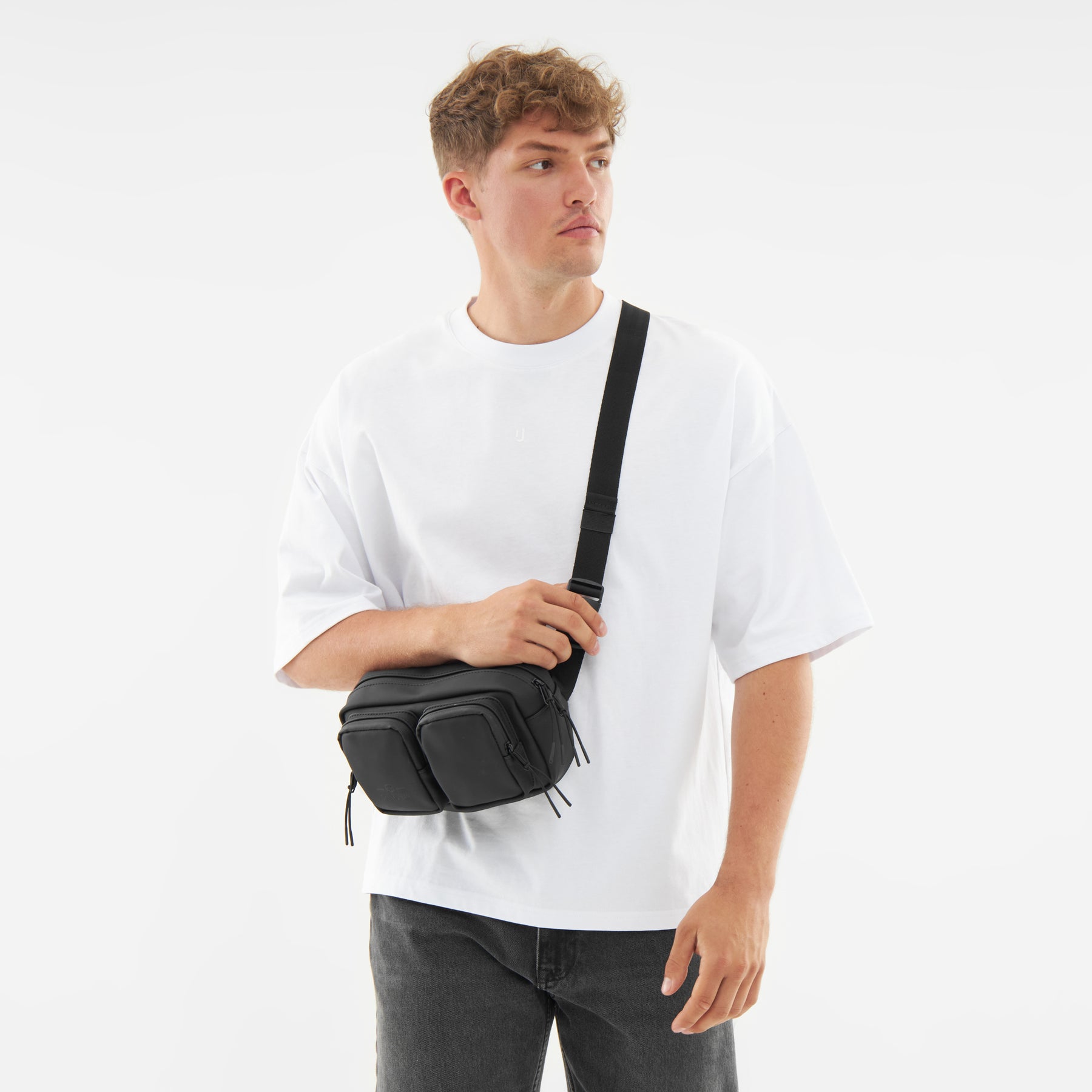 Mann trägt schwarze Umhängetasche 'Wesley' quer über dem Oberkörper, weiße T-Shirt, schwarze Hose