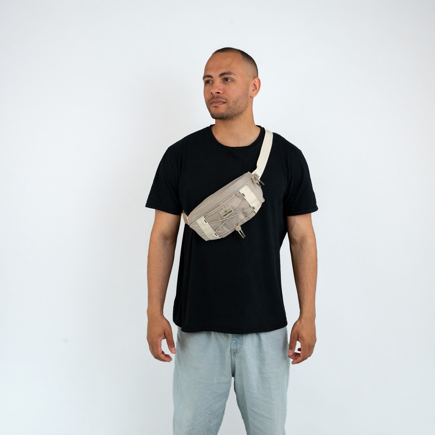 Mann trägt beige Bauchtasche 'Devin' von Johnny Urban quer über der Brust, schwarzes T-Shirt und helle Hose