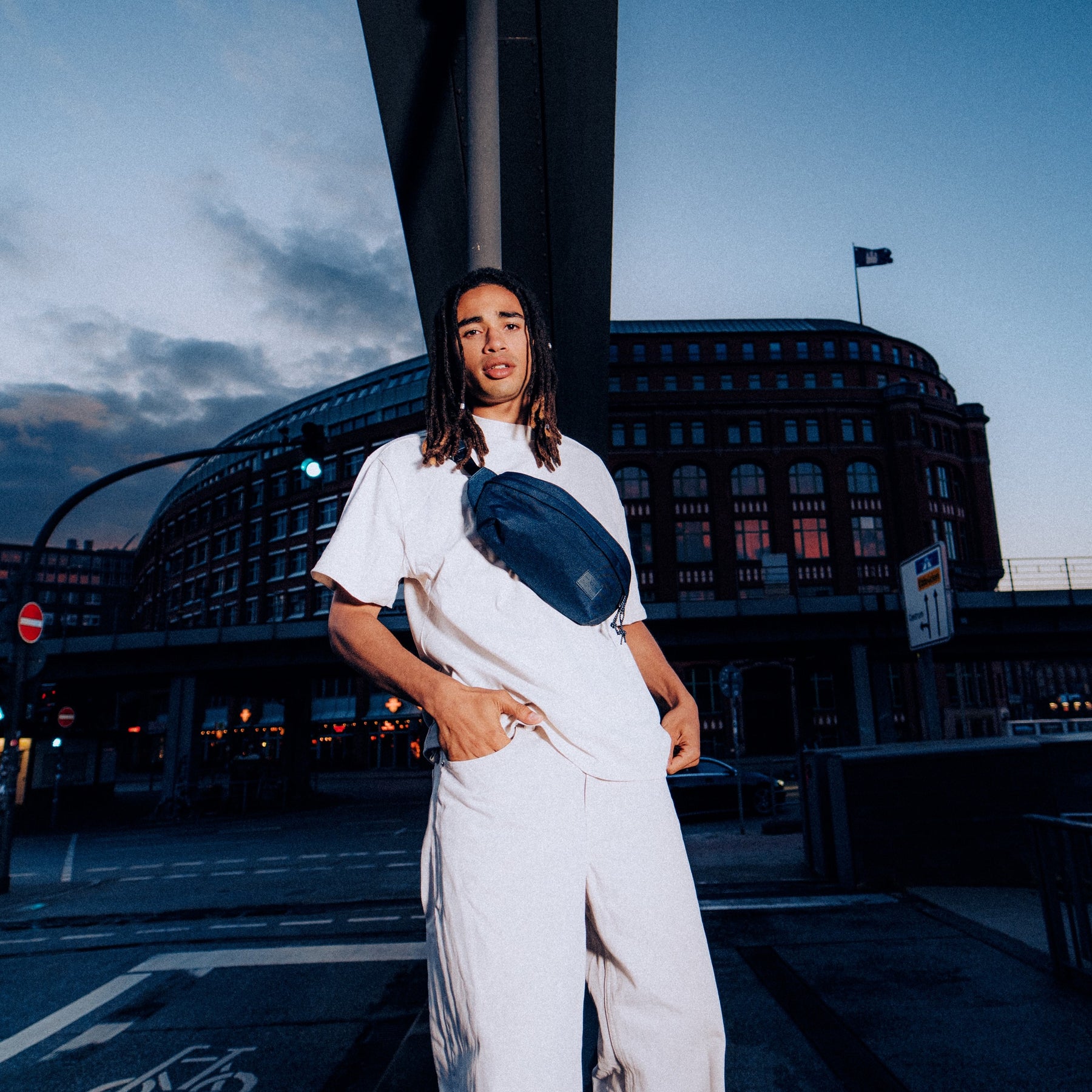 Mann mit blauer Johnny Urban Bauchtasche 'Tom' über weißem T-Shirt in urbaner Abendumgebung