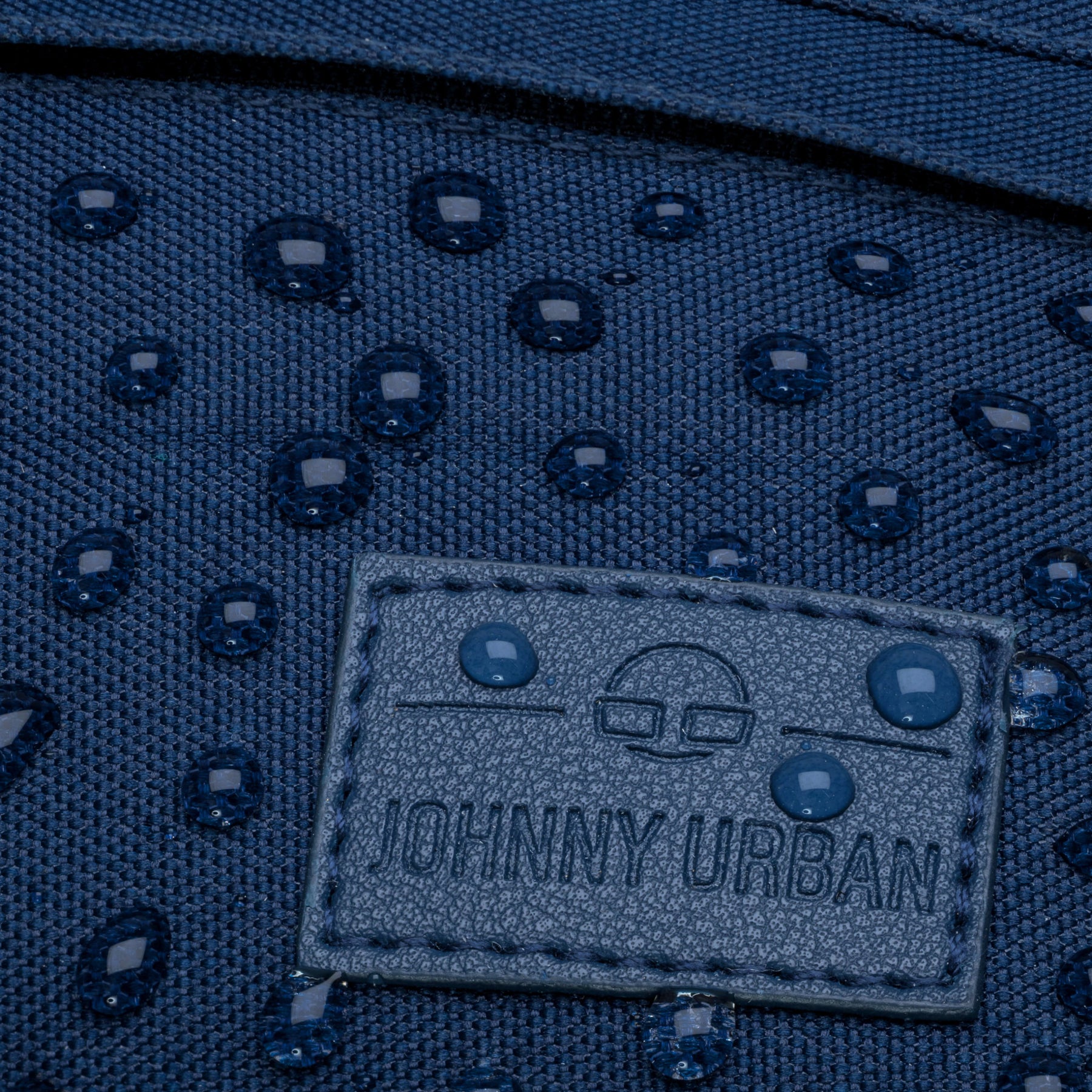 Nahaufnahme einer blauen, wasserabweisenden Bauchtasche 'Tom' von Johnny Urban mit Wassertropfen