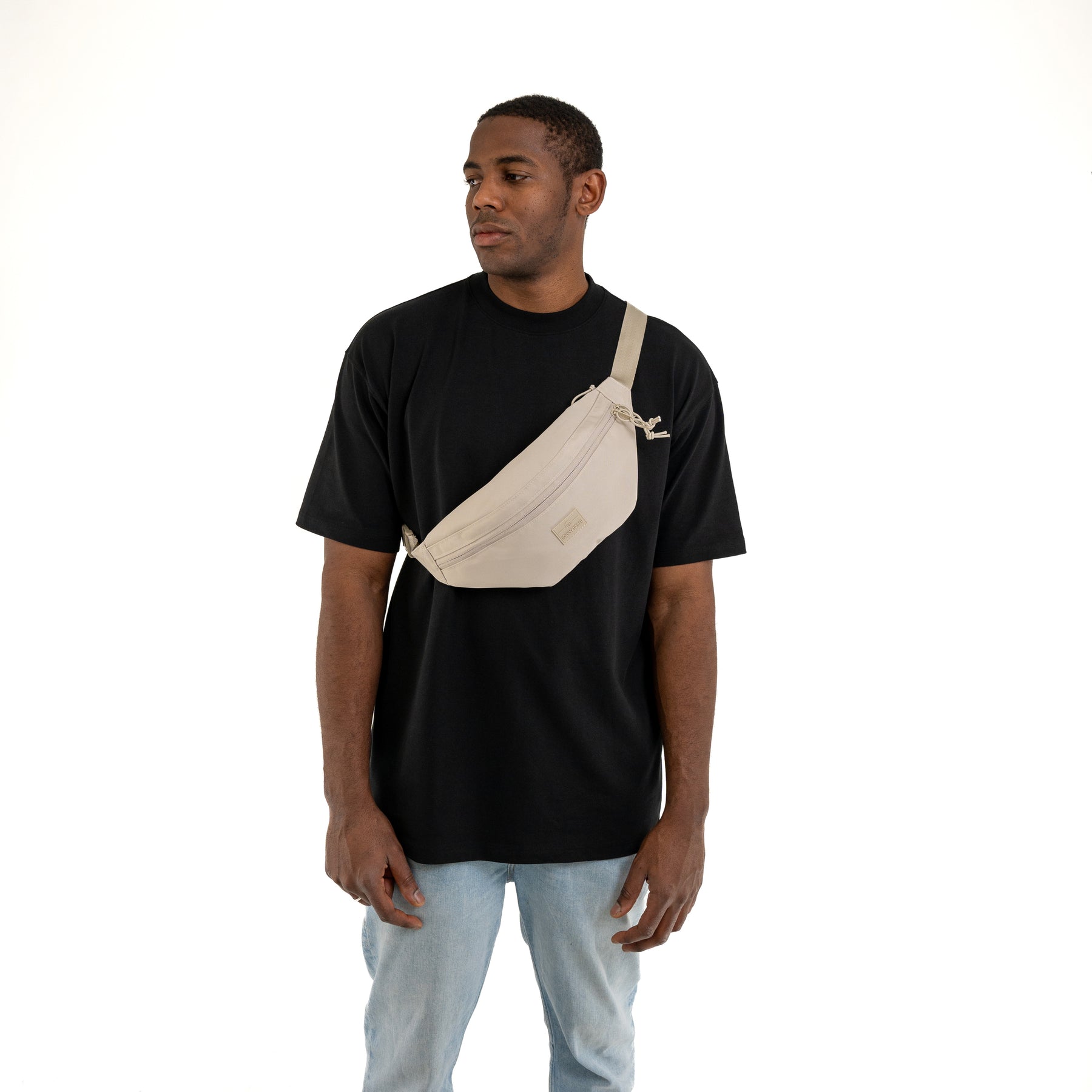 Mann trägt beige Bauchtasche 'Erik Large' von Johnny Urban quer über der Brust zu schwarzem T-Shirt und blauen Jeans