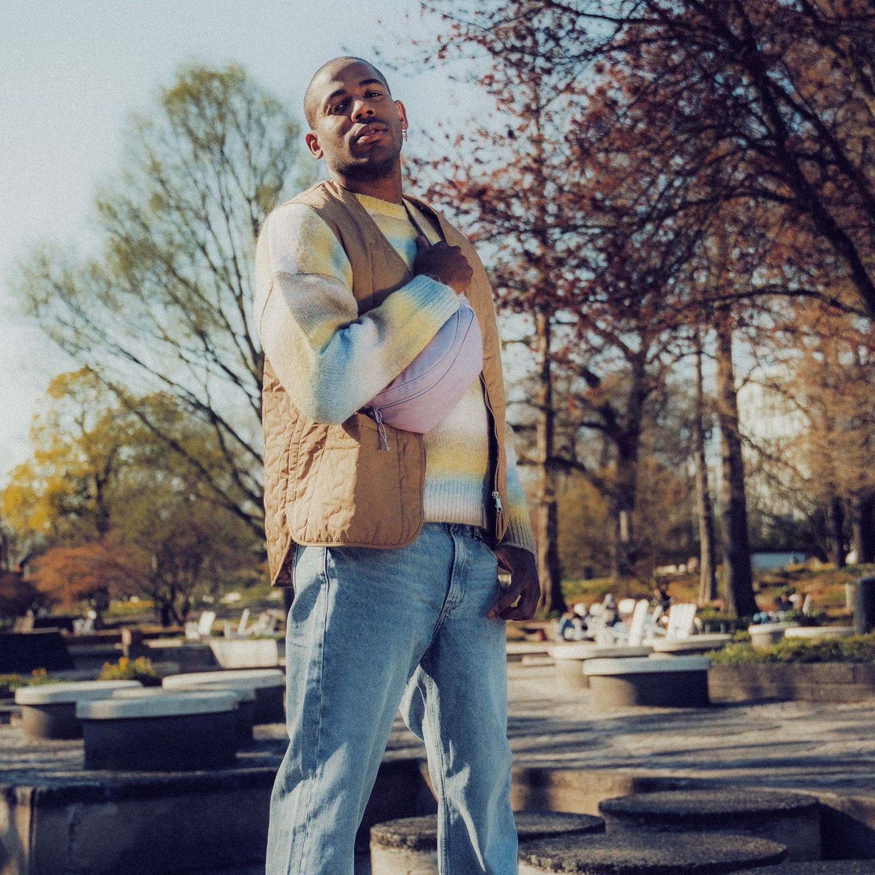 Mann trägt lila Kunstleder-Bauchtasche 'Toni' über Pullover und Weste im Park