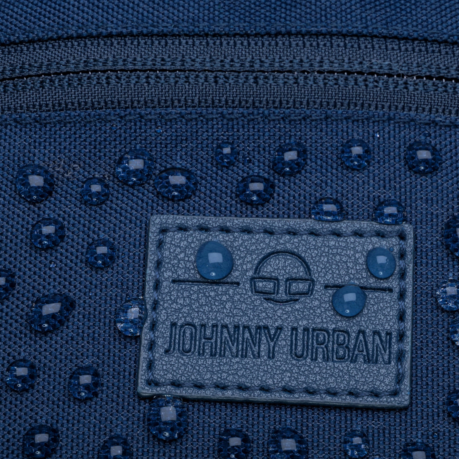 Detailaufnahme der wasserabweisenden blauen Bauchtasche „Erik Small“ von Johnny Urban mit sichtbaren Wassertropfen und Markenlabel