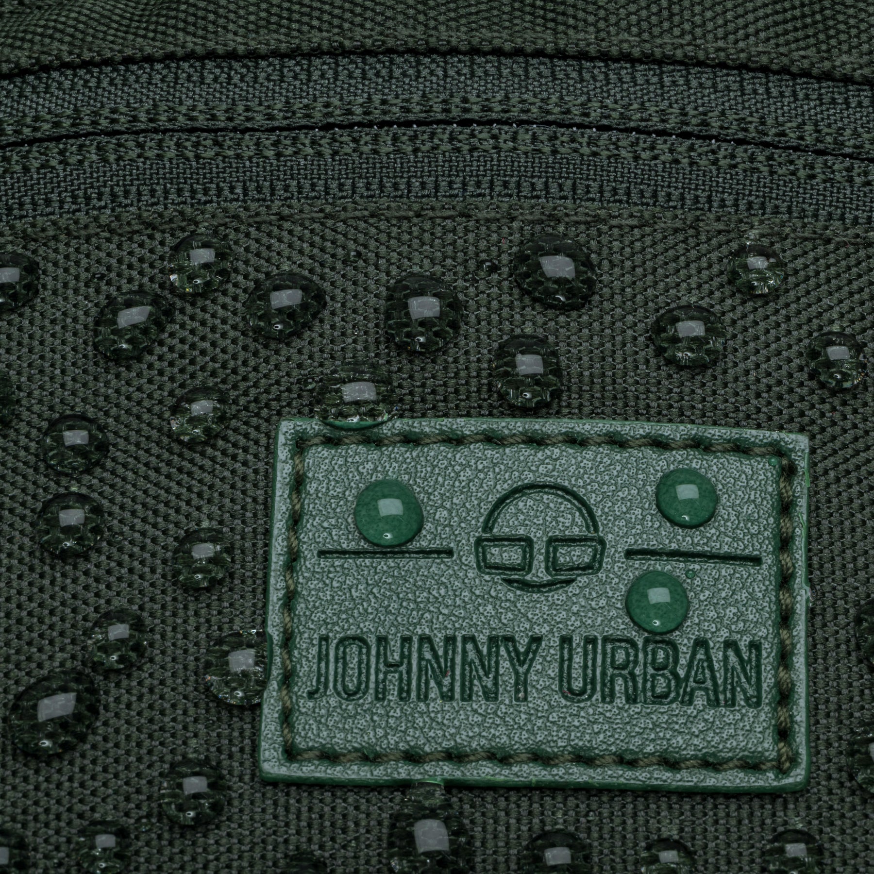 Nahaufnahme der wasserabweisenden grünen Johnny Urban Bauchtasche 'Erik Small' mit Wassertropfen auf dem Logo