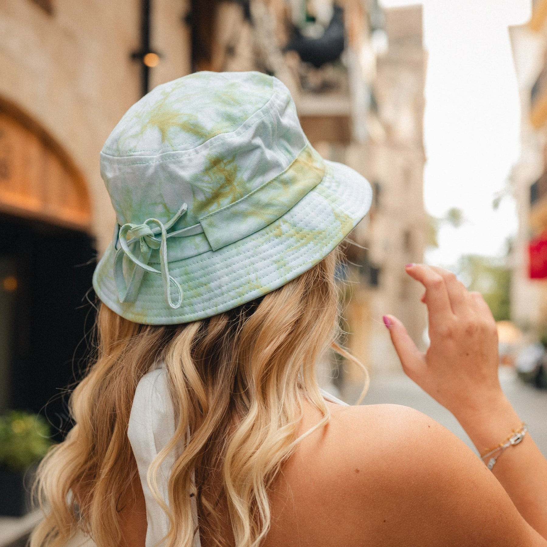 Frau trägt Bucket Hat 'Gill' von Johnny Urban in pastellfarbenem Batikmuster, Rückansicht in urbaner Umgebung