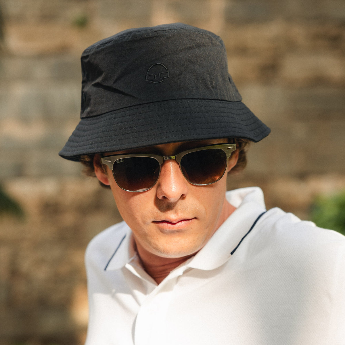 Mann trägt schwarzen Bucket Hat 'Bob' von Johnny Urban und Sonnenbrille, weißes Polohemd