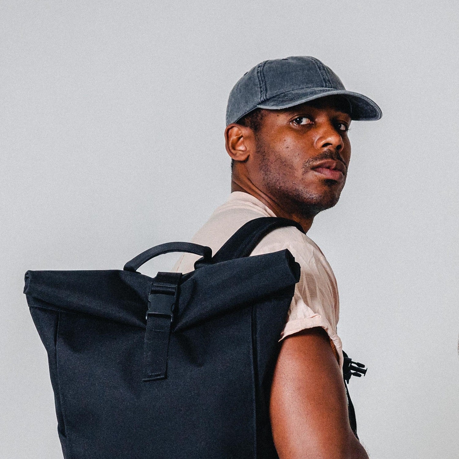 Mann trägt schwarze rollbare Rucksacktasche und graue Cap 'Dave'