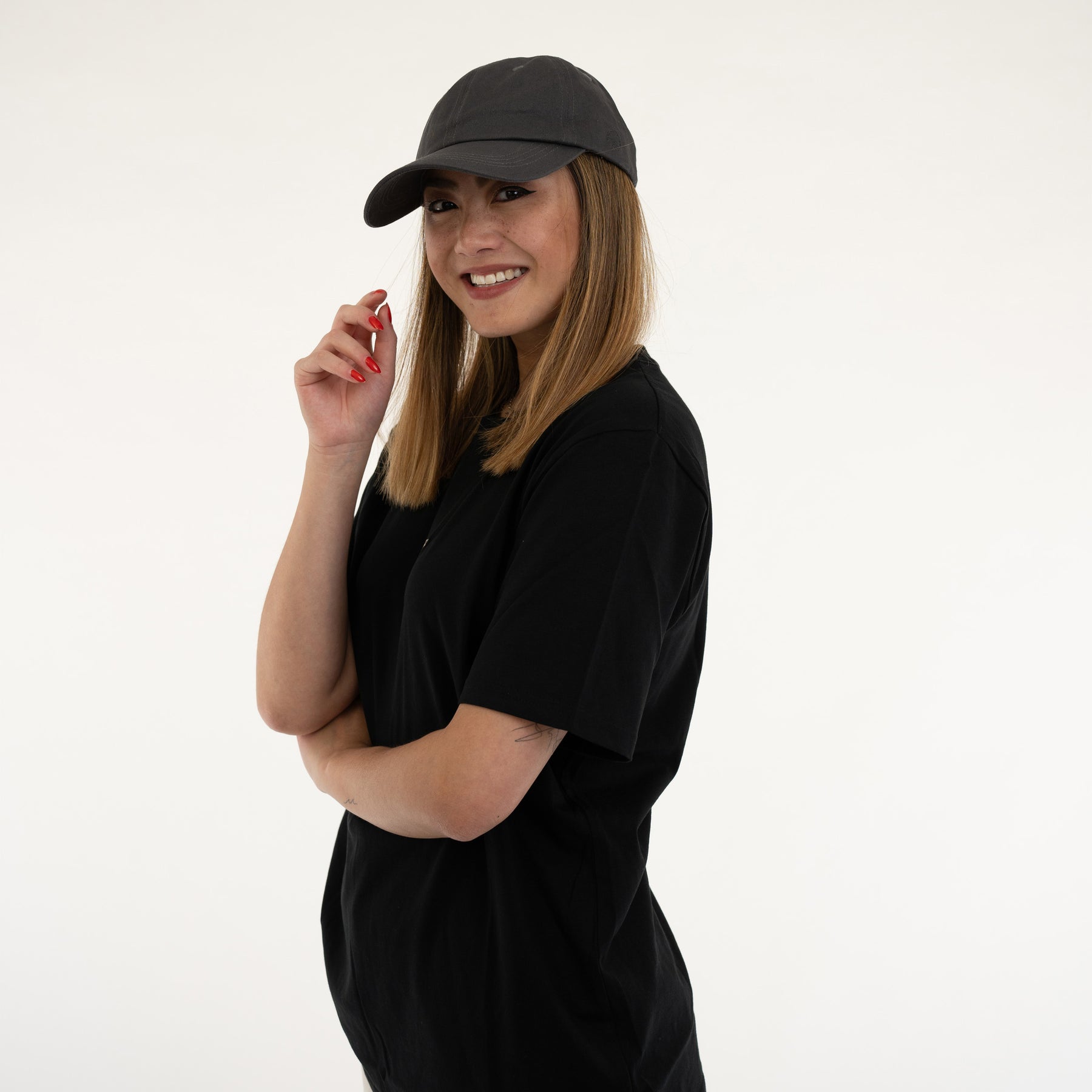 Frau trägt dunklegraue Cap 'Jen' und schwarzes T-Shirt, lächelnd, mittellange Haare