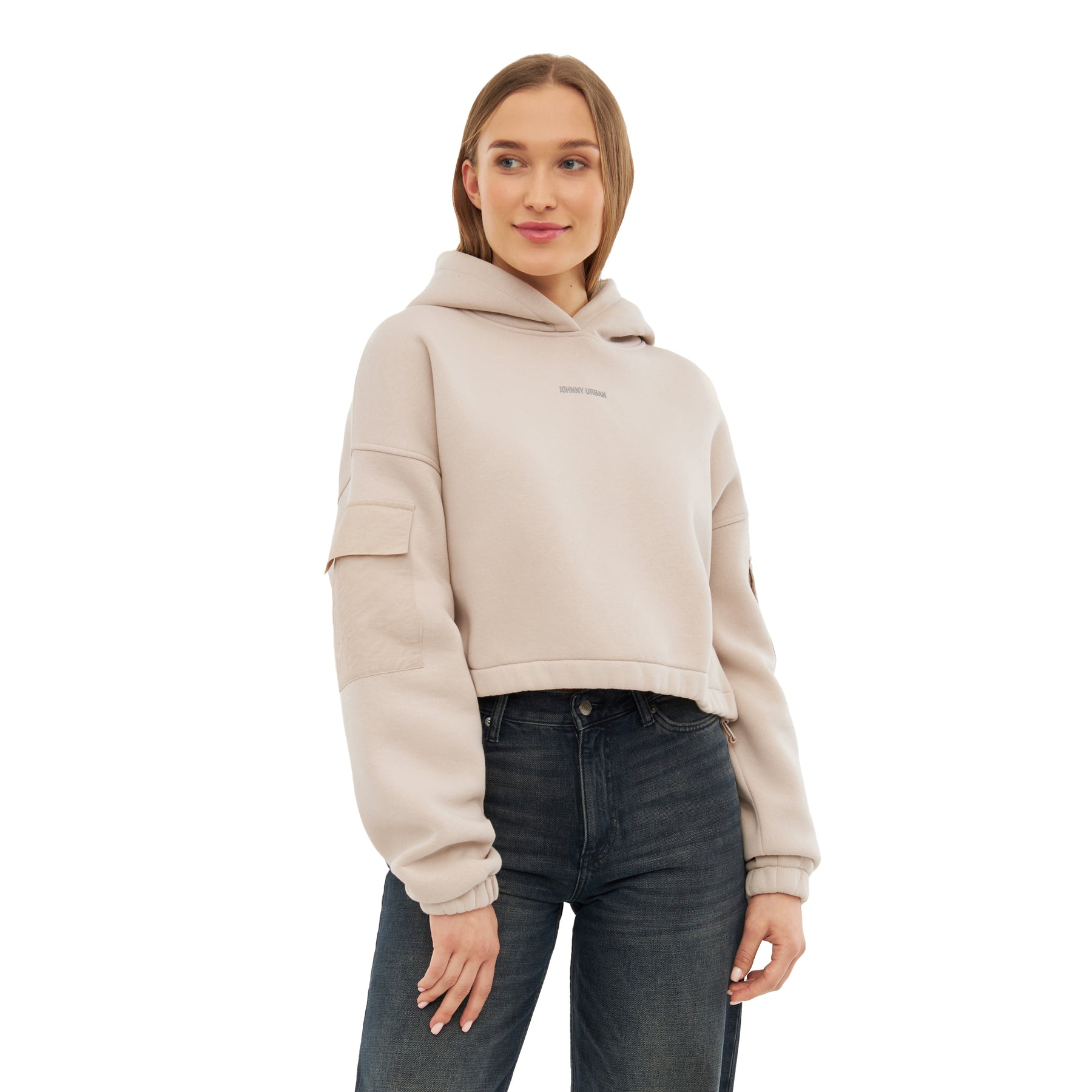 Frau trägt hellbeige Cropped Hoodie 'Carly' mit Kapuze und Taschen auf den Ärmeln, kombiniert mit dunklen Jeans
