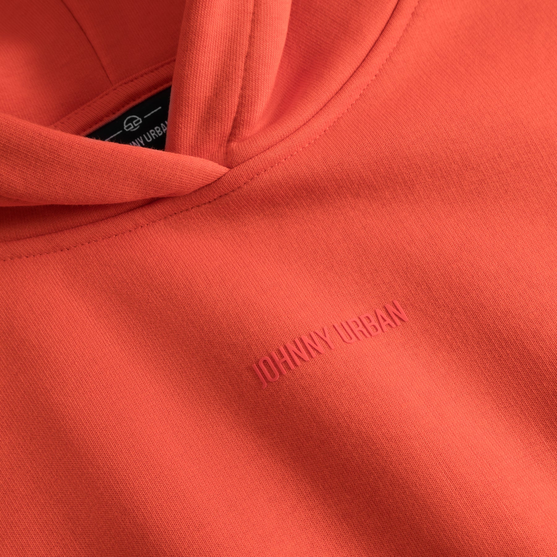 Detailaufnahme eines orangen Cropped Hoodies 'Carly' mit eingeprägtem Schriftzug 'Johnny Urban'