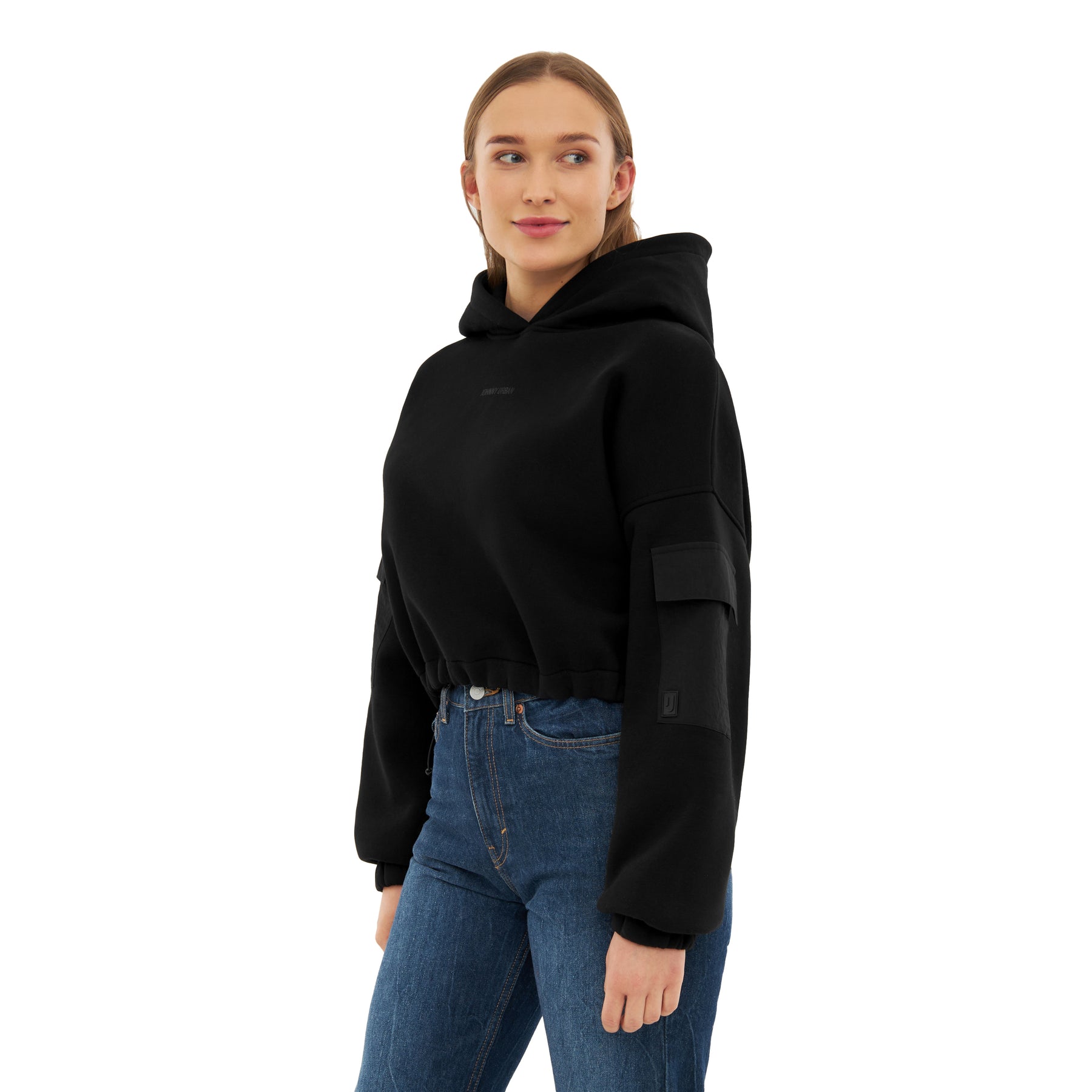 Frau trägt schwarzen Cropped Hoodie 'Carly' mit Kapuze und Tasche am Ärmel, kombiniert mit blauen Jeans