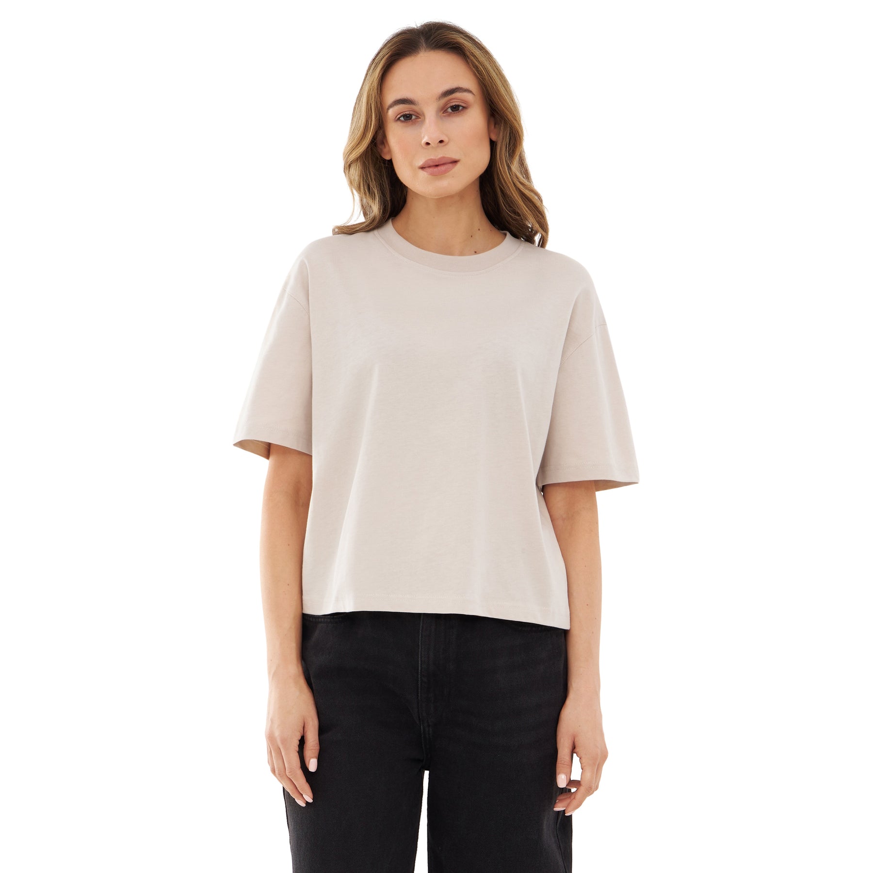 Frau mit beige Cropped T-Shirt 'Zoey' und schwarzen Hosen, stehend vor weißem Hintergrund