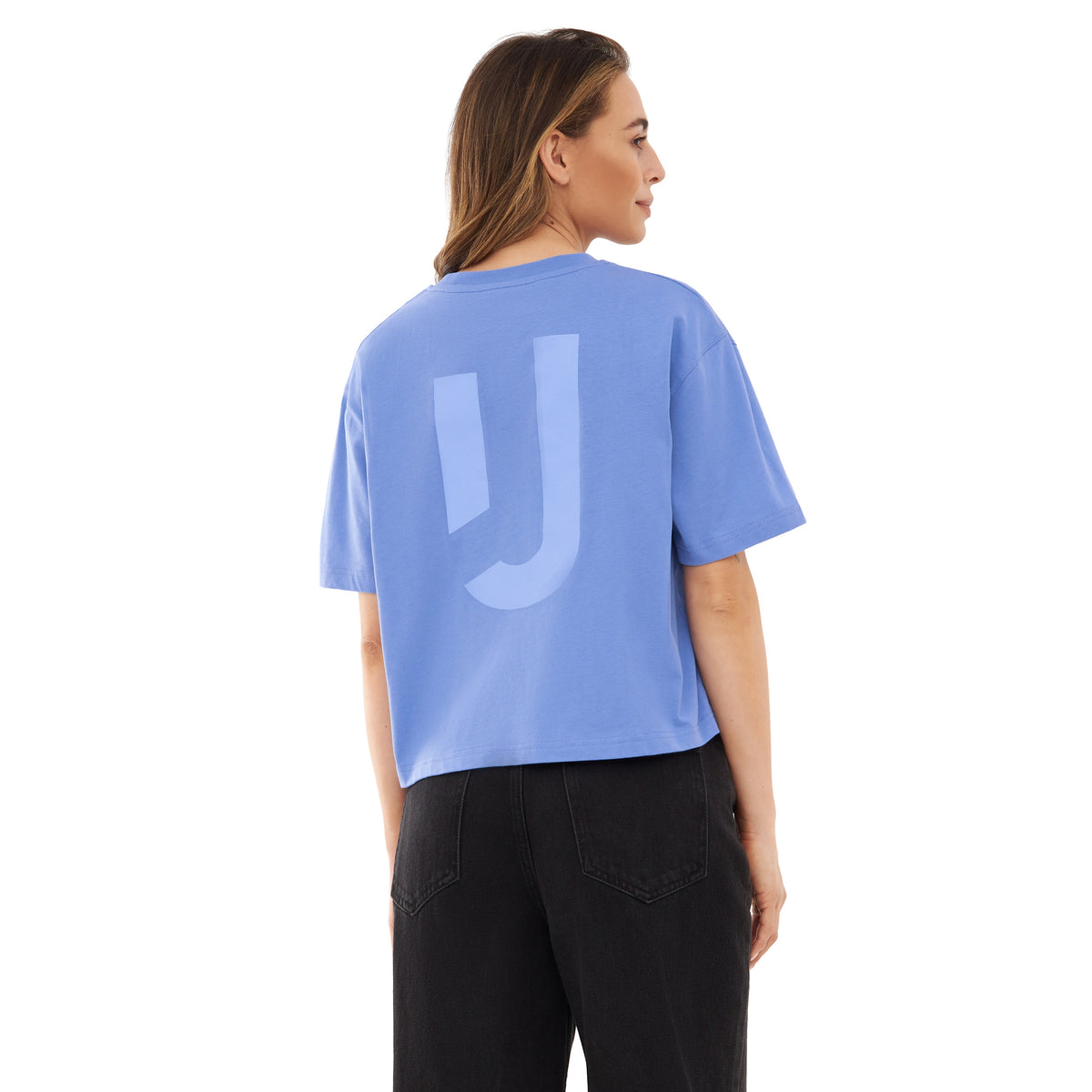 Frau trägt oversized cropped T-Shirt 'Zoey JU' in Blau mit lila Print vom Rücken