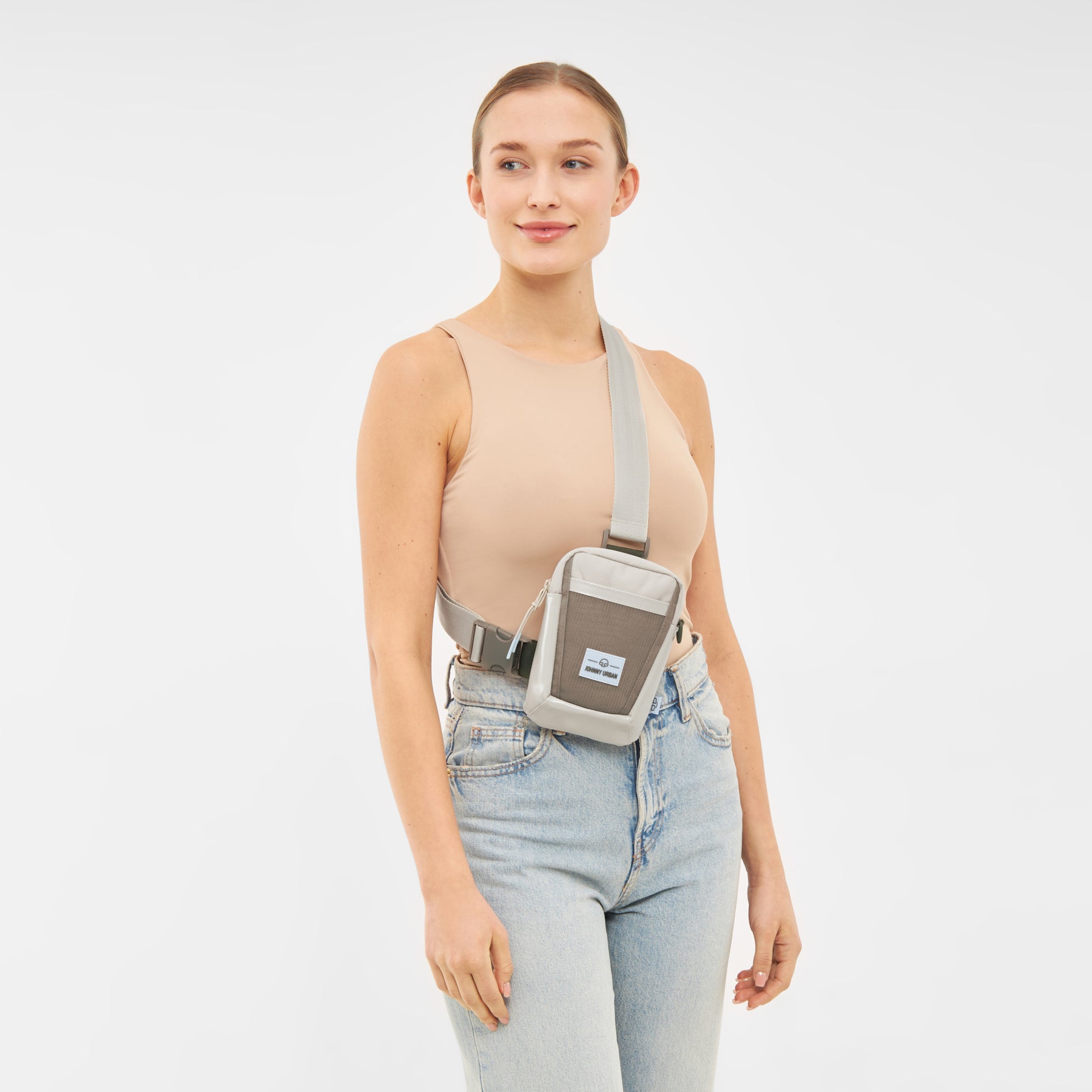 Frau trägt die Johnny Urban Umhängetasche 'Lex' in Grau über dem Oberkörper zu beiger Ärmelloser Top und blauen Jeans