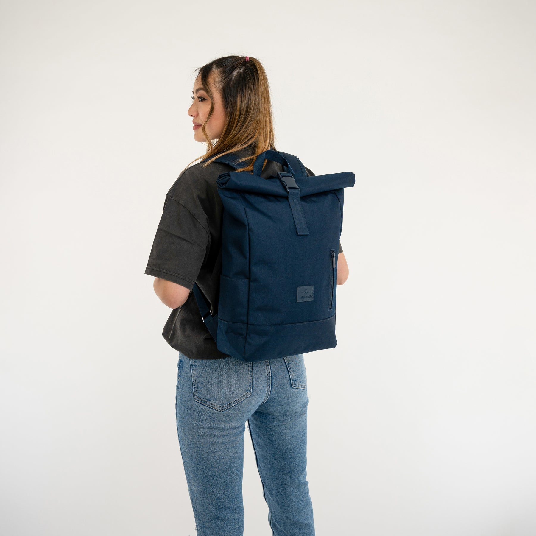Frau trägt dunkelblauen Rolltop Rucksack 'Robin Medium' von Johnny Urban mit schwarzem T-Shirt und blauer Jeans
