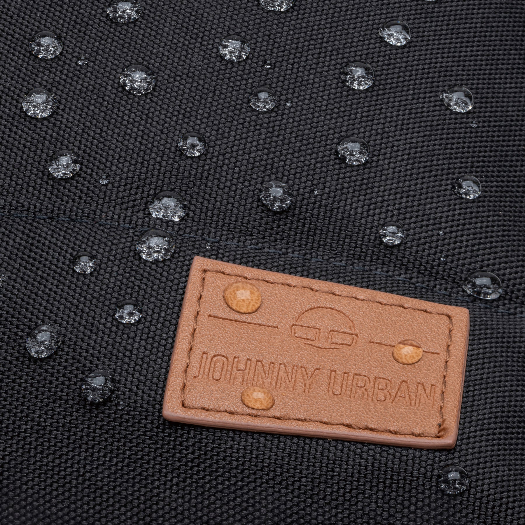 Wasserabweisendes schwarzes Material mit braunem Lederetikett 'Johnny Urban' und Wassertropfen darauf