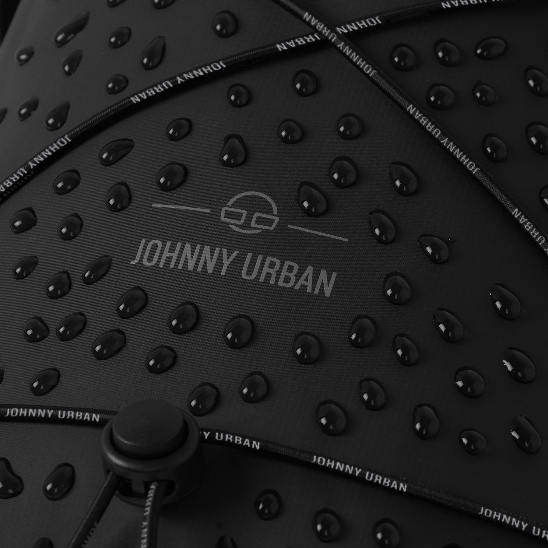 Nahe Aufnahme der wasserabweisenden Oberfläche der schwarzen Dry Bag 'Theo' von Johnny Urban mit Tropfen und Kordelzug