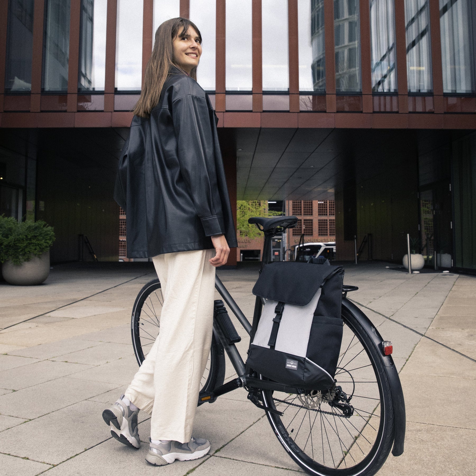 Frau neben Fahrrad mit reflektierendem Rucksack 'Mika' von Johnny Urban am Gepäckträger