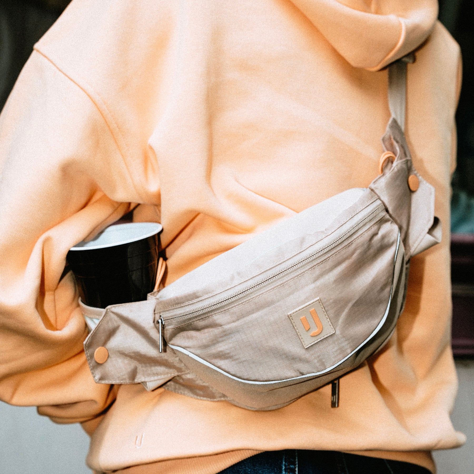 Beige 2in1 Bauchtasche 'Jimmy' von Johnny Urban mit Flaschenhalter, getragen über einem hellorangenen Hoodie