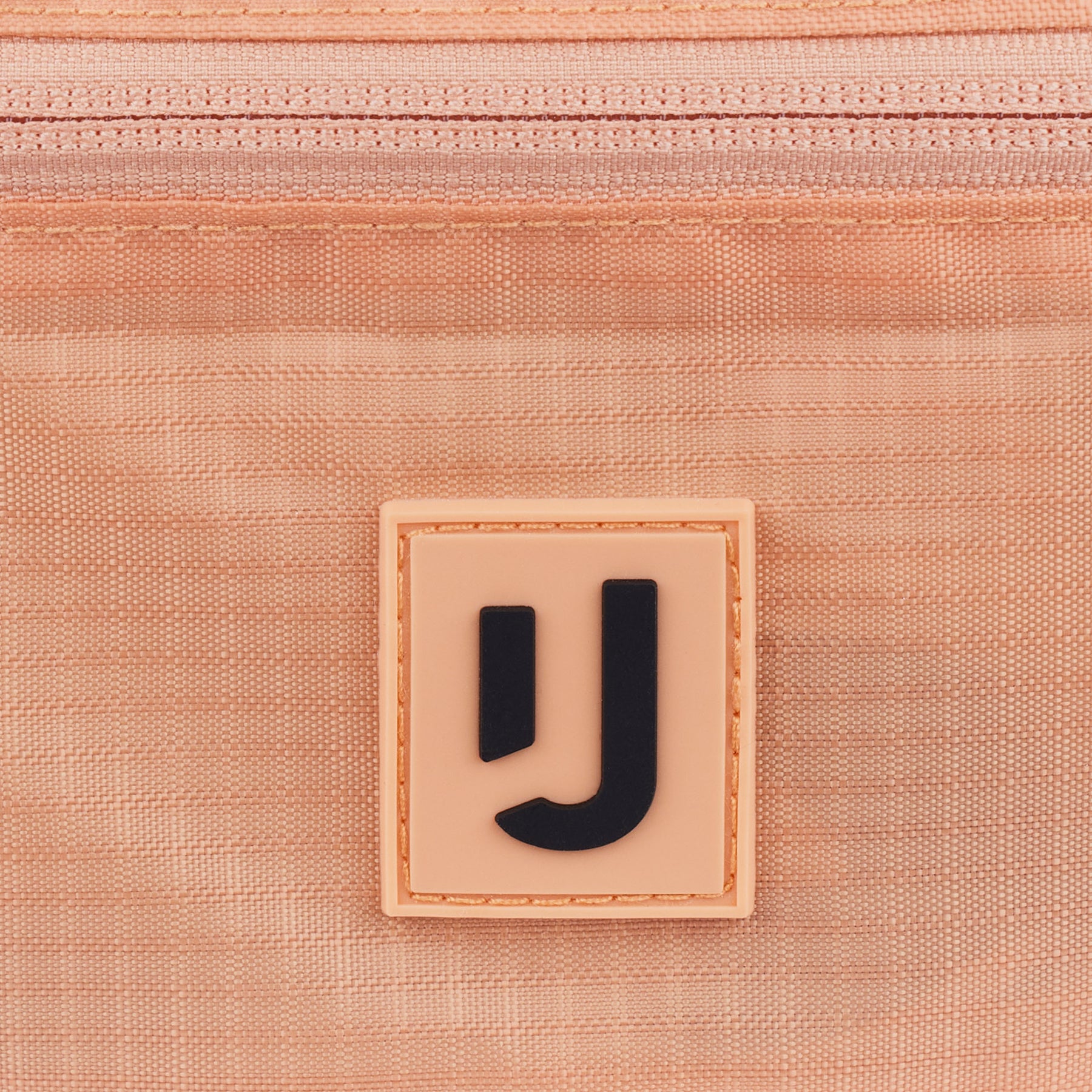 Nahe Aufnahme des Johnny Urban Logos auf der wasserabweisenden 2in1 Bauchtasche 'Jimmy' in Peach-Farbe