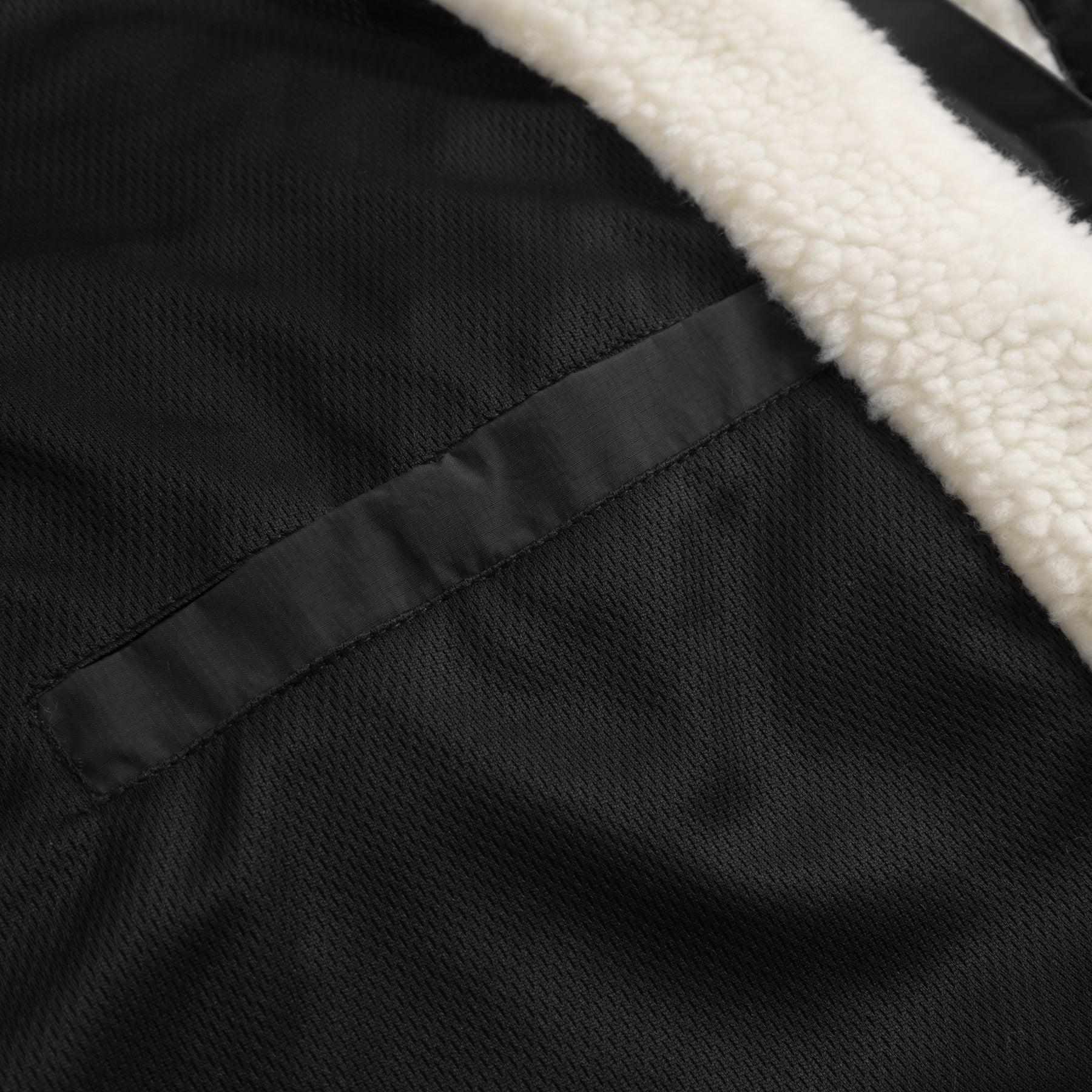 Nahaufnahme eines schwarzen Taschenverschlusses und cremefarbener Teddyfleece-Innenseite der Teddy Fleecejacke 'Carson'