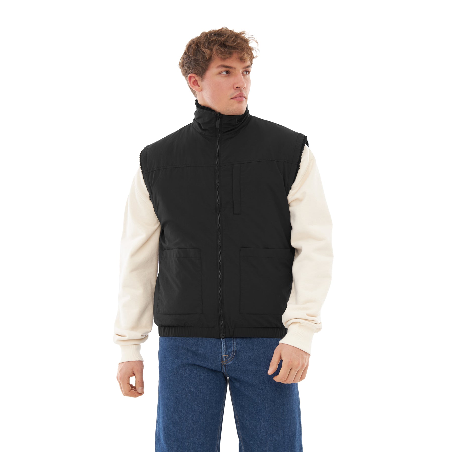 Mann trägt schwarze, moderne, wendbare Teddy Fleeceweste 'Bryson' über cremefarbenem Pullover und blauen Jeans