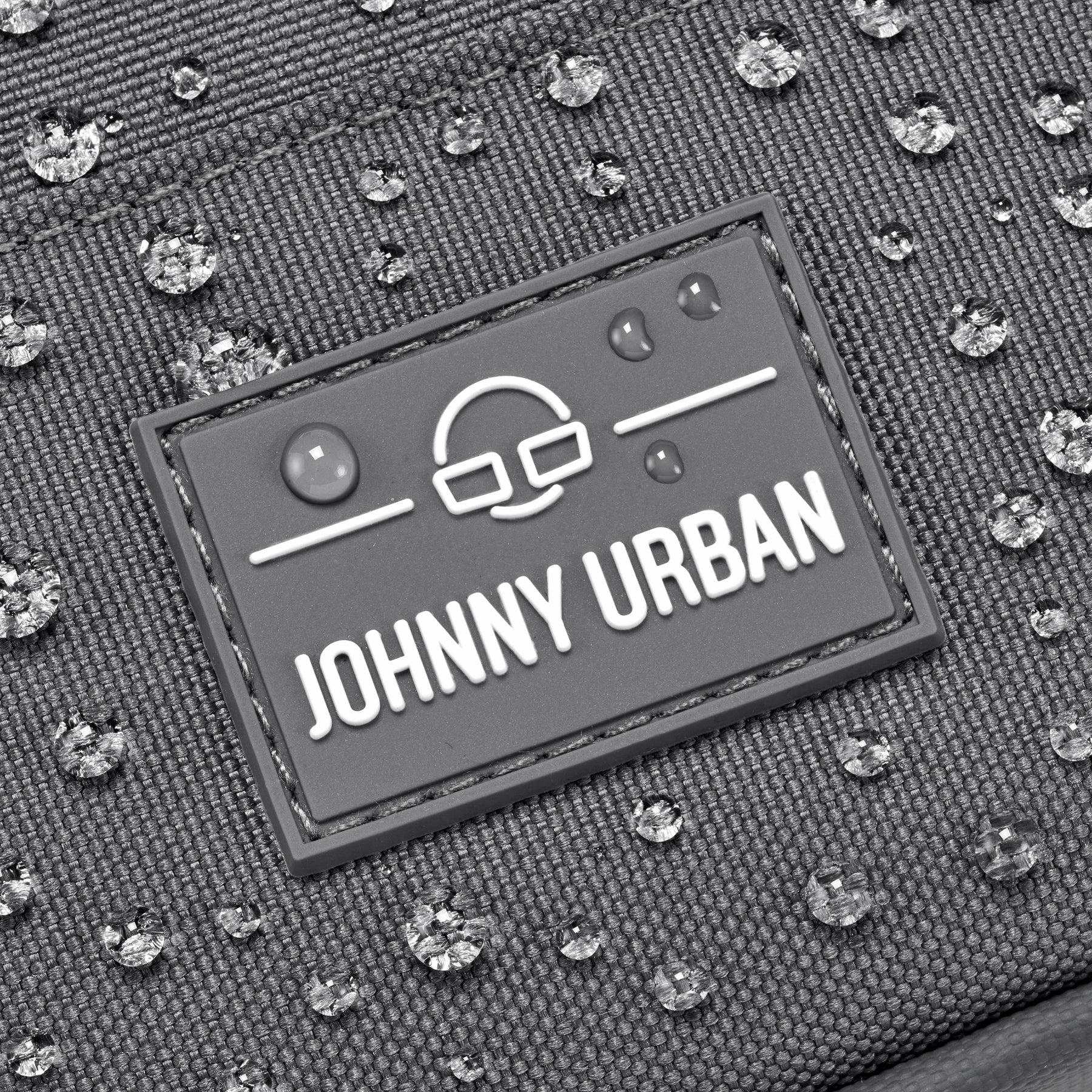 Nahaufnahme des Johnny Urban Logos auf wasserabweisendem Front Pack 'Arthur' mit Wassertröpfchen