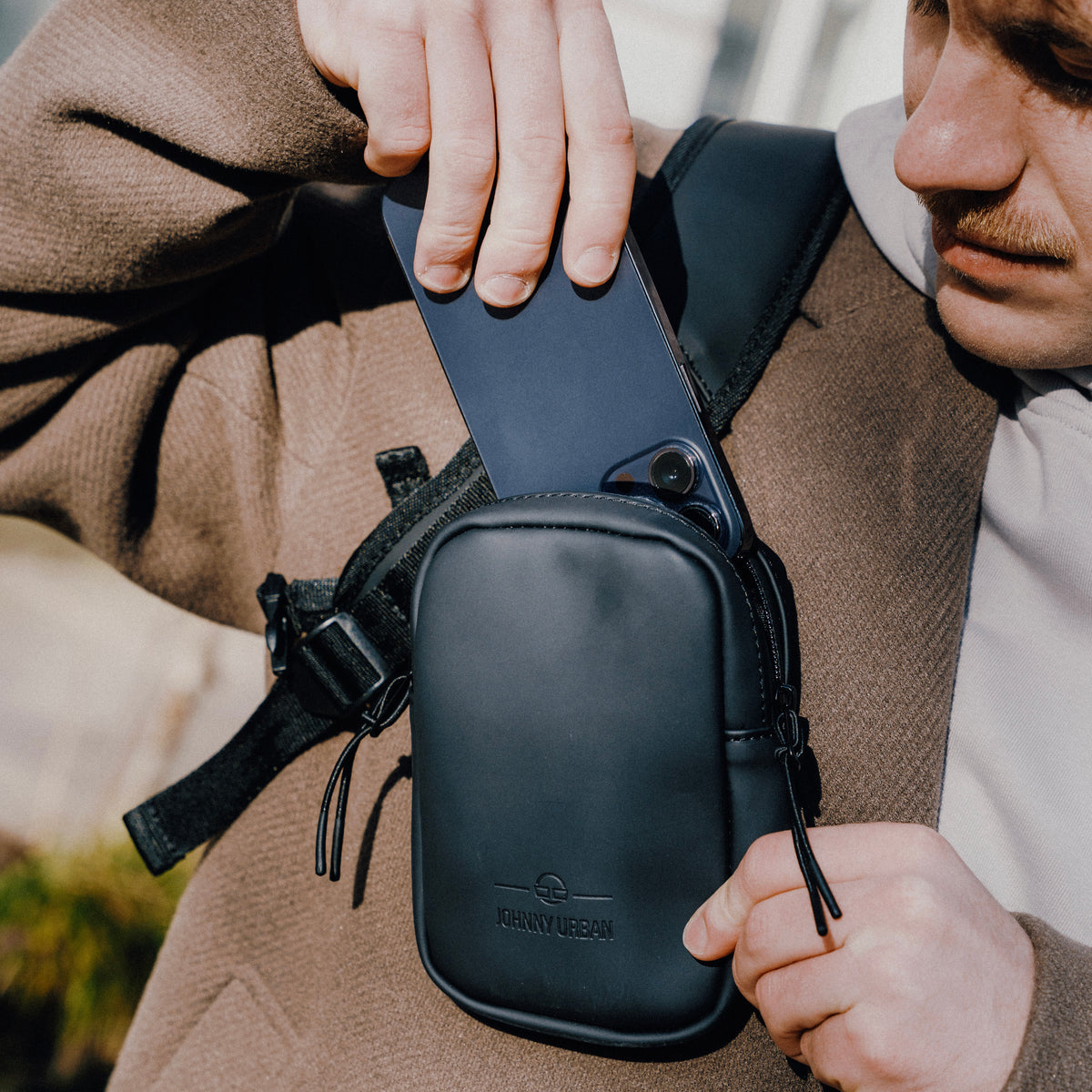 Person steckt ein Smartphone in das schwarze Front Pack 'Toby' von Johnny Urban