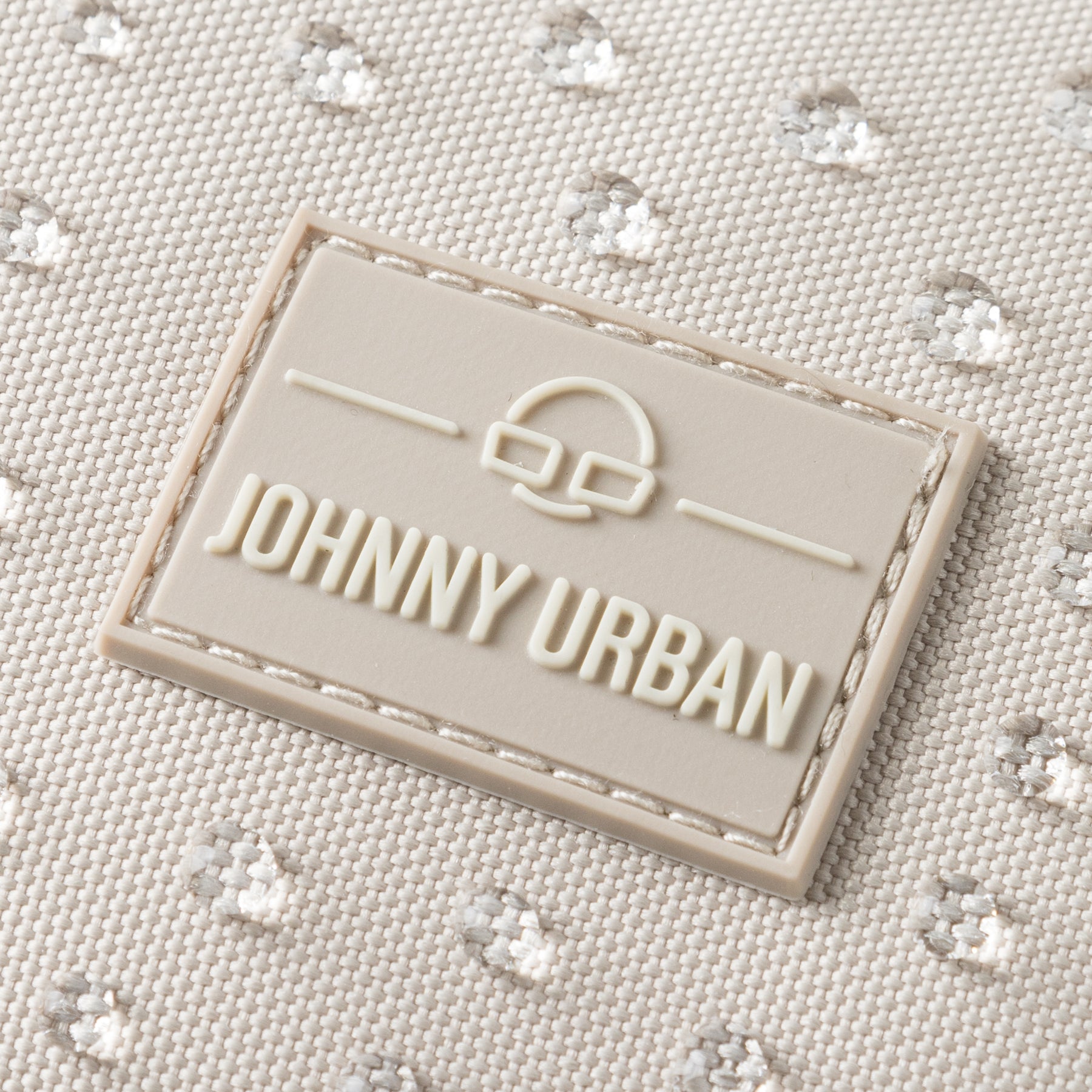Nahaufnahme des Johnny Urban Logos auf sandfarbenem, wasserabweisendem Stoff mit kleiner Punktstruktur