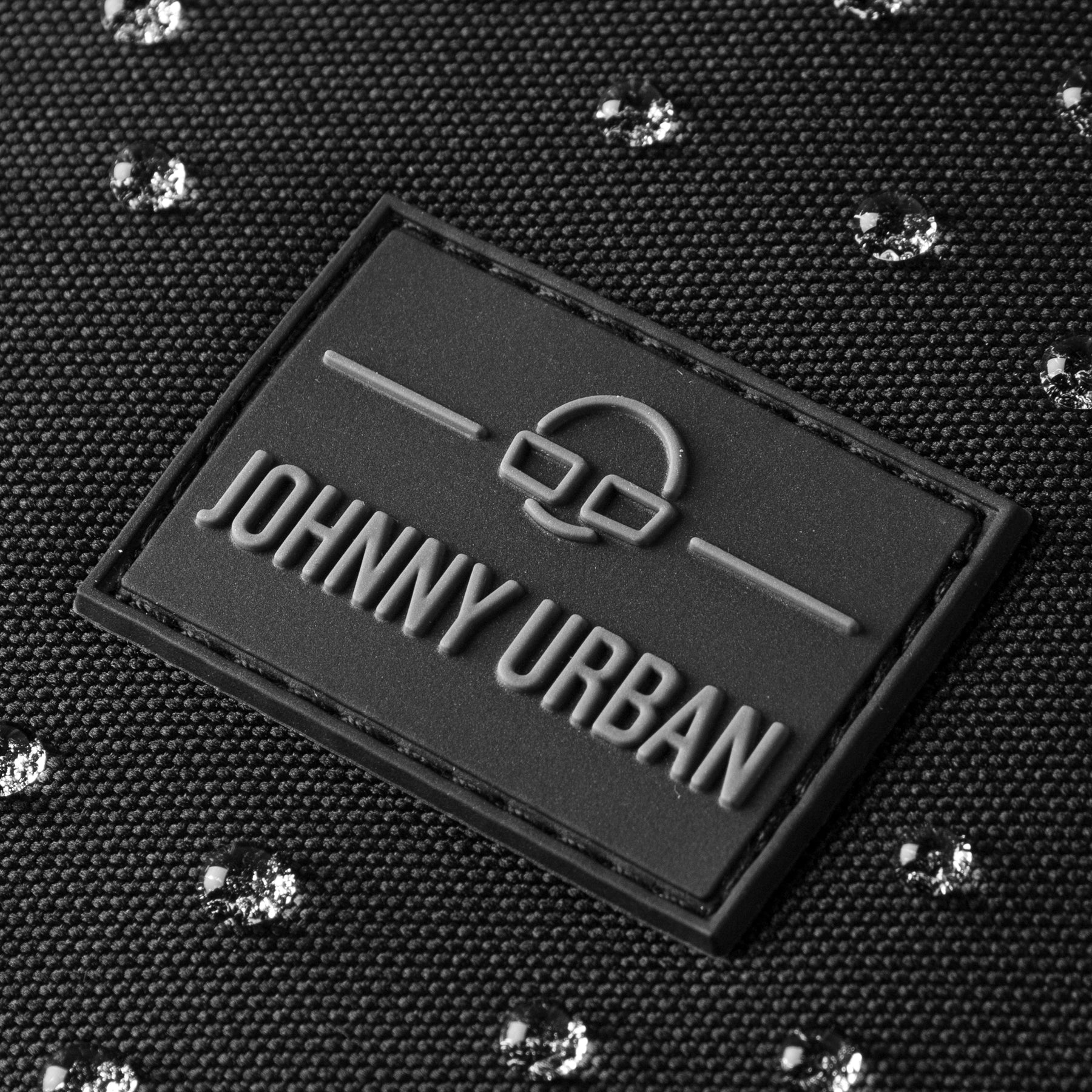 Nahe Aufnahme des schwarzen Johnny Urban Logos auf wasserabweisendem Stoff mit glänzenden Wassertropfen