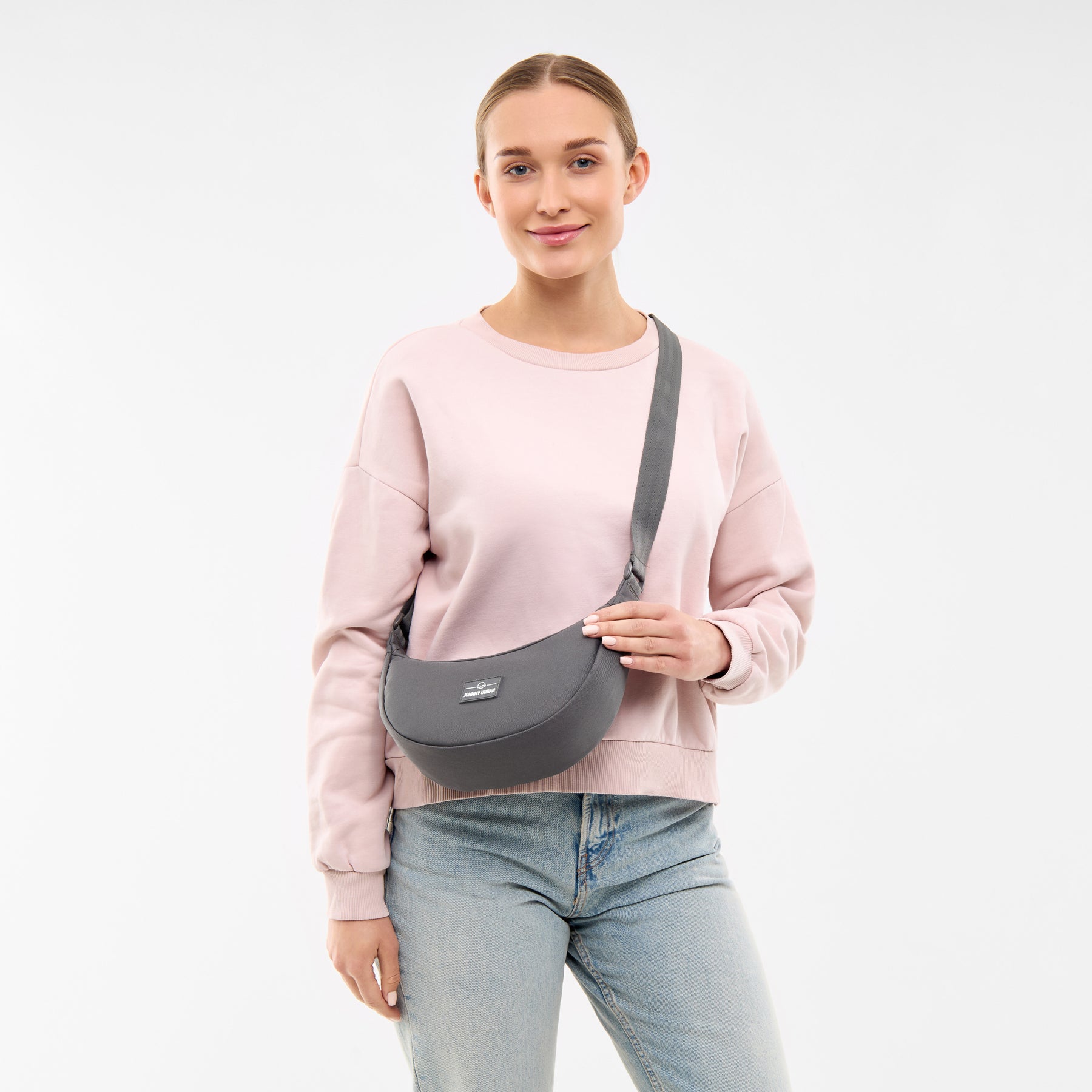 Frau mit dunkelgrauer Half Moon Bag 'Ally Small' von Johnny Urban, trägt rosa Pullover und Jeans