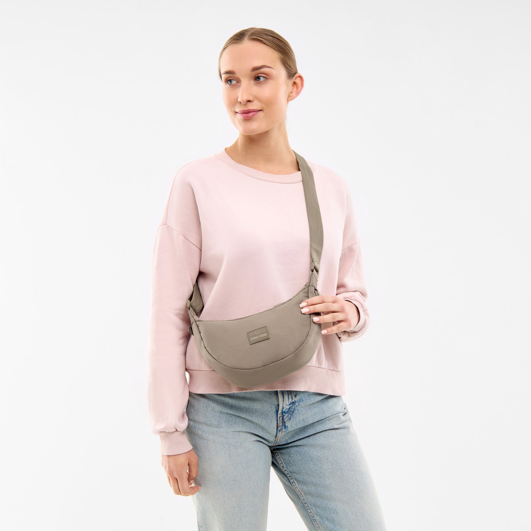 Frau trägt Half Moon Bag 'Ally Small' in desert grey, kombiniert mit hellem Pullover und Jeans