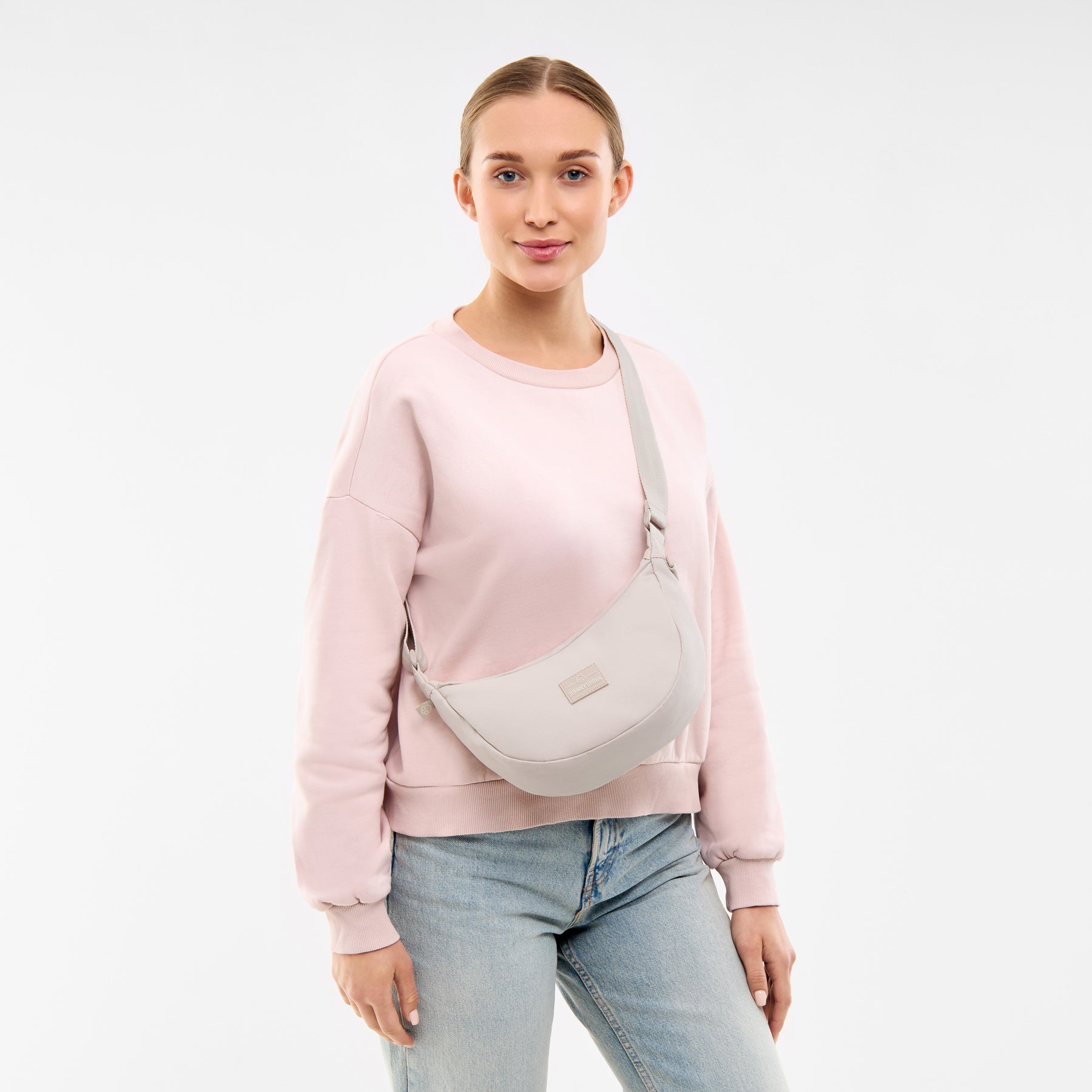 Frau trägt Half Moon Bag 'Ally Small' in Sandfarben, kombiniert mit hellem Pullover und Jeans