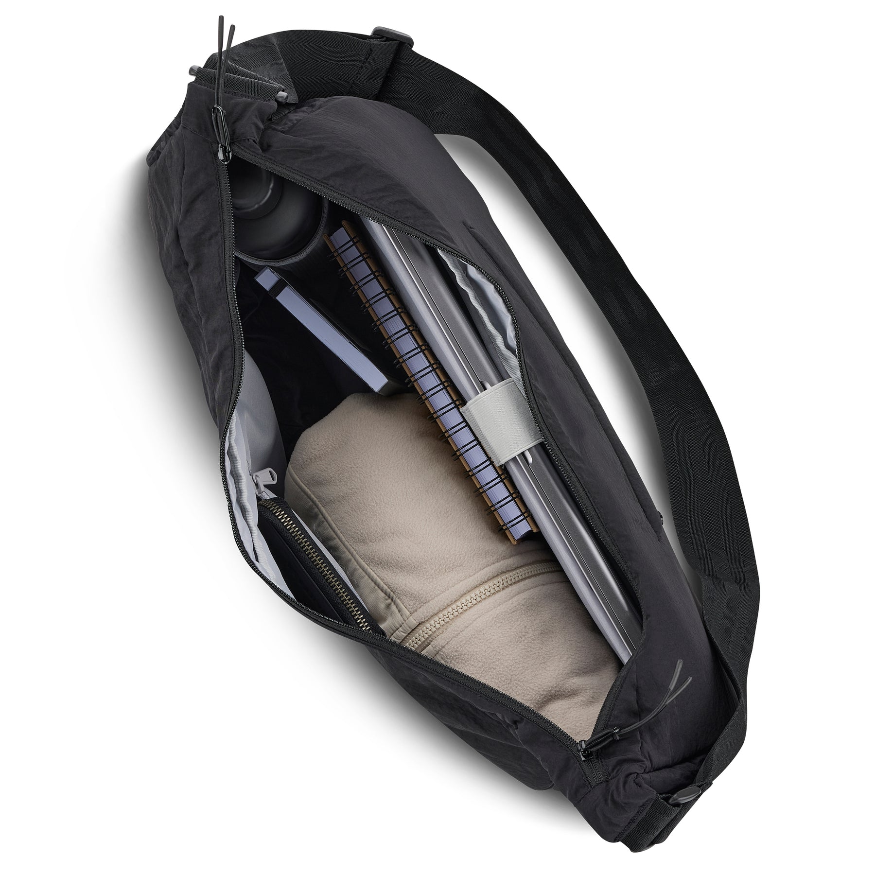 Schwarze Half Moon Bag 'Kaia XL' mit Reißverschluss, gefüllt mit Laptop, Notizbuch, Trinkflasche und beige Jacke