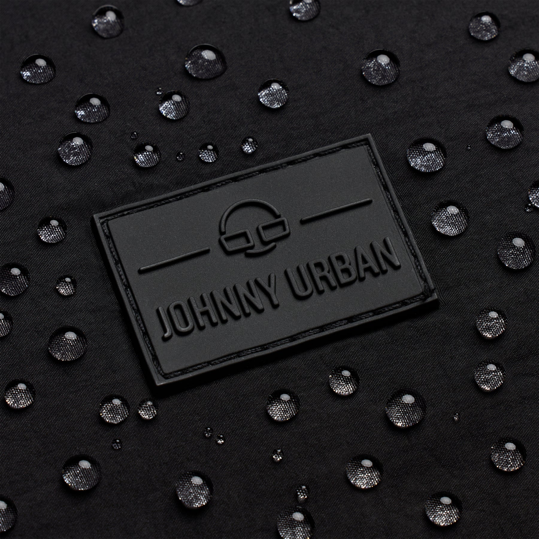 Schwarzes geprägtes Johnny Urban Logo auf wasserabweisendem Material mit Wassertropfen