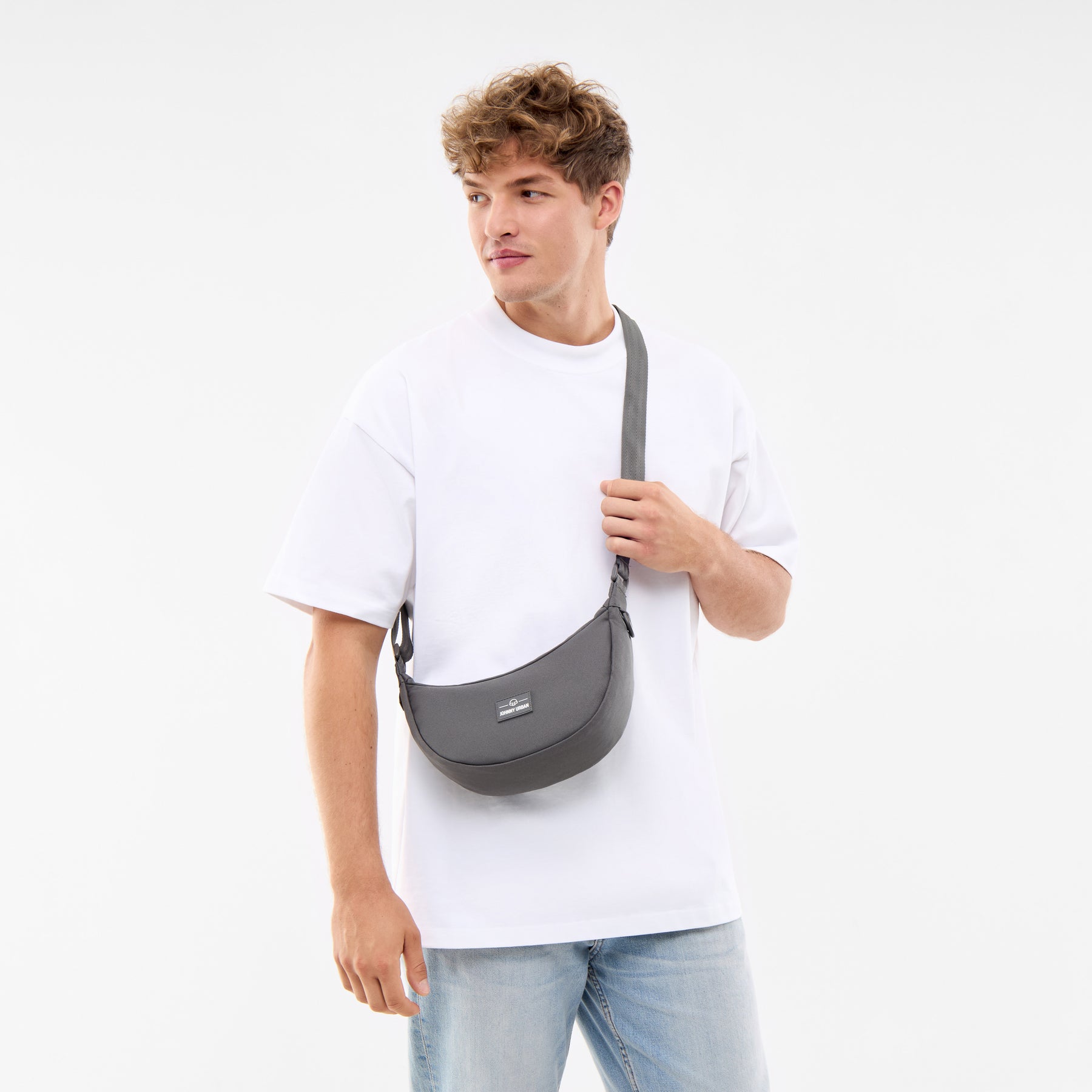 Mann trägt Half Moon Bag 'Ally Small' in dunklem Grau über der Schulter, kombiniert mit weißem T-Shirt und hellblauen Jeans