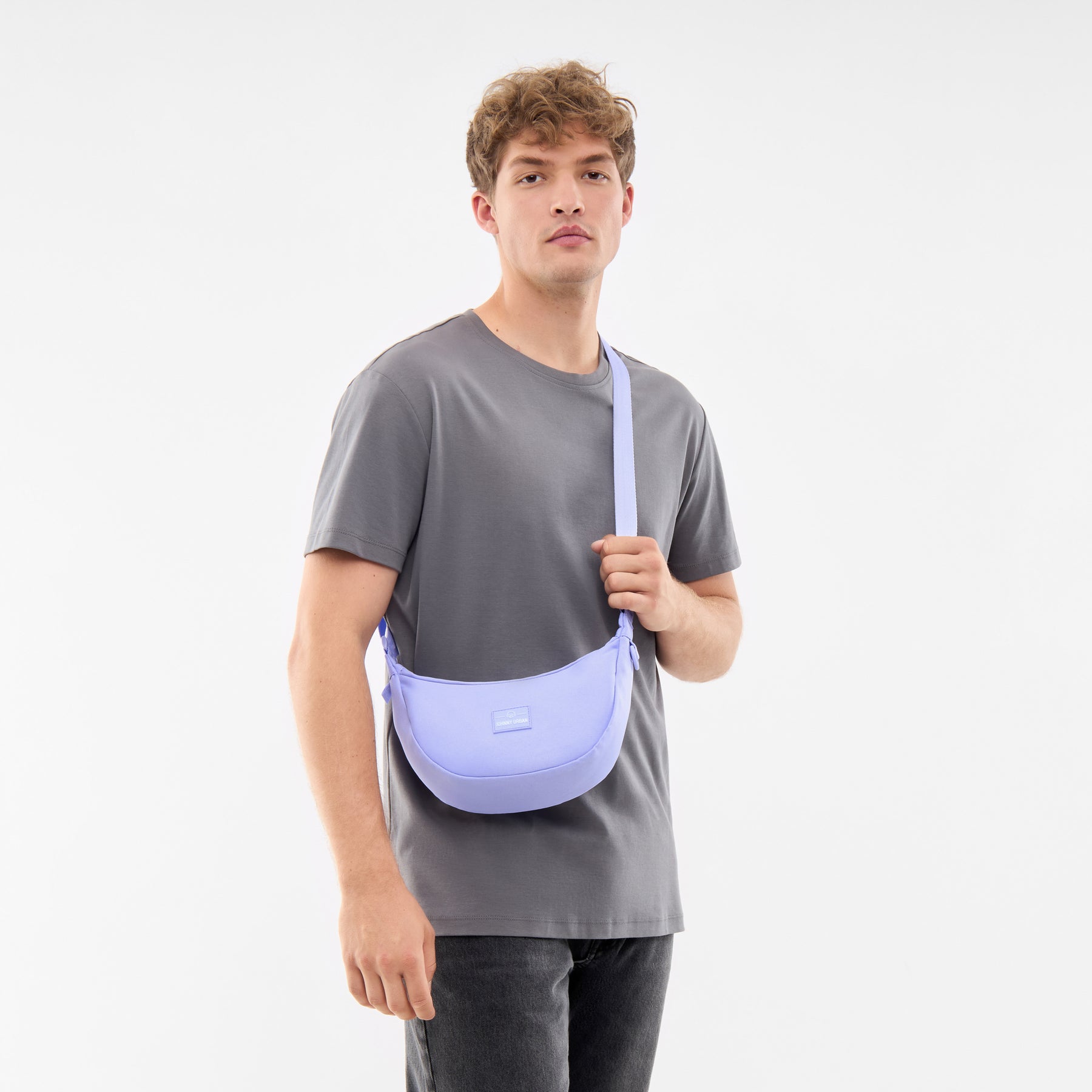 Mann trägt Half Moon Bag ‚Ally Small‘ in fliederfarbenem Nylon als Umhängetasche