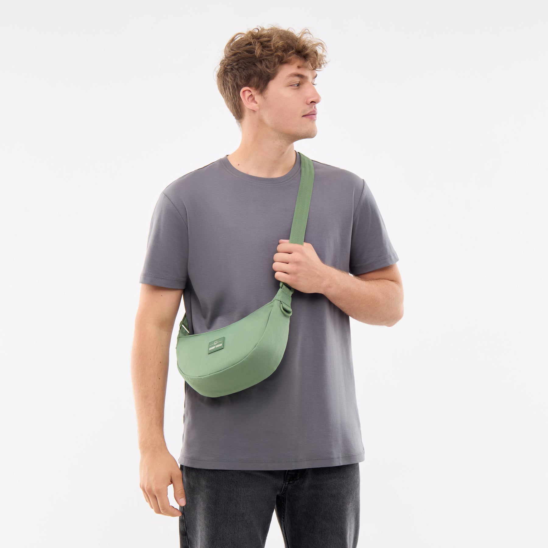 Mann trägt halbmondförmige kleine Umhängetasche 'Ally Small' in Salbeigrün von Johnny Urban