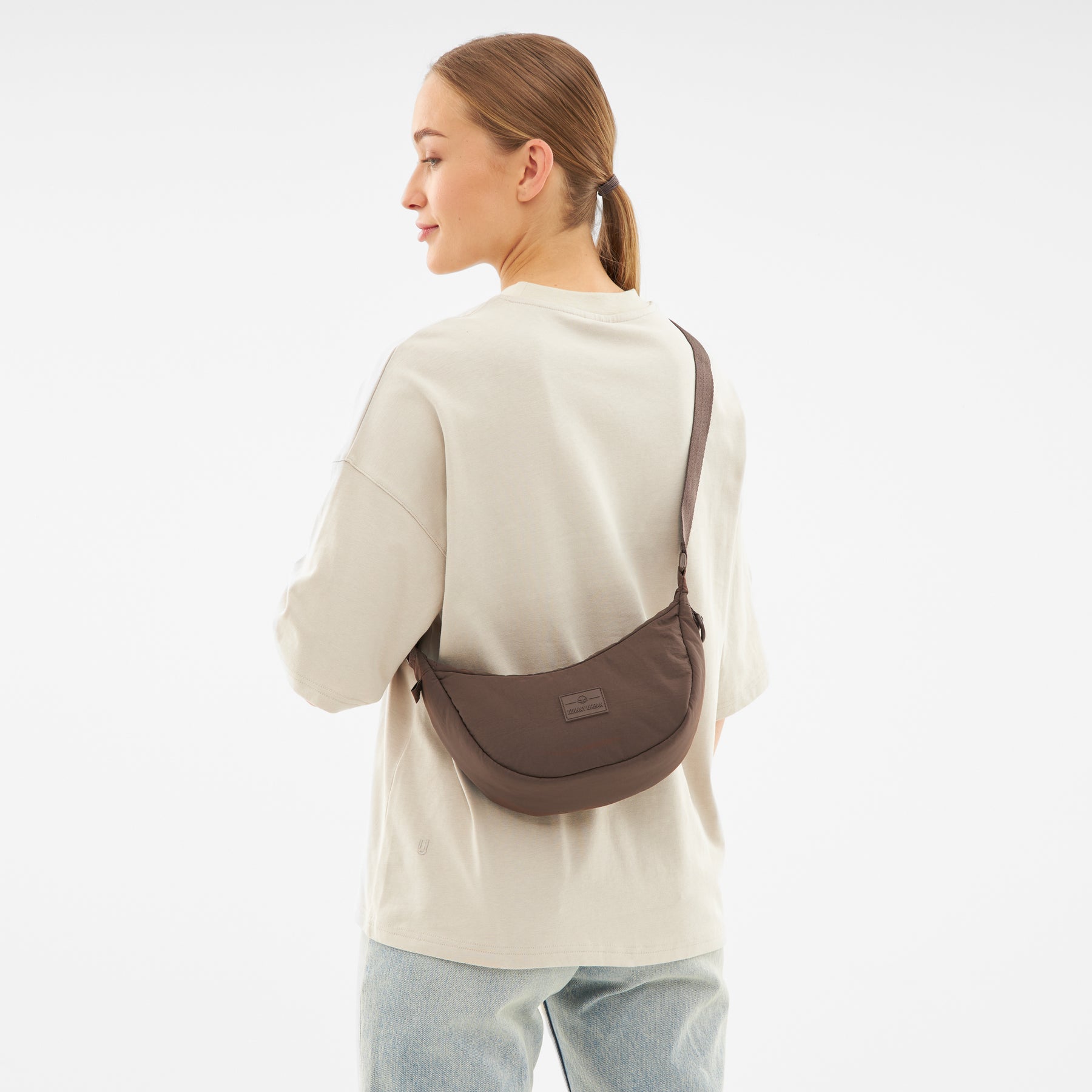 Frau mit halbrund geformter brauner Half Moon Bag 'Kaia Small' von Johnny Urban über der Schulter