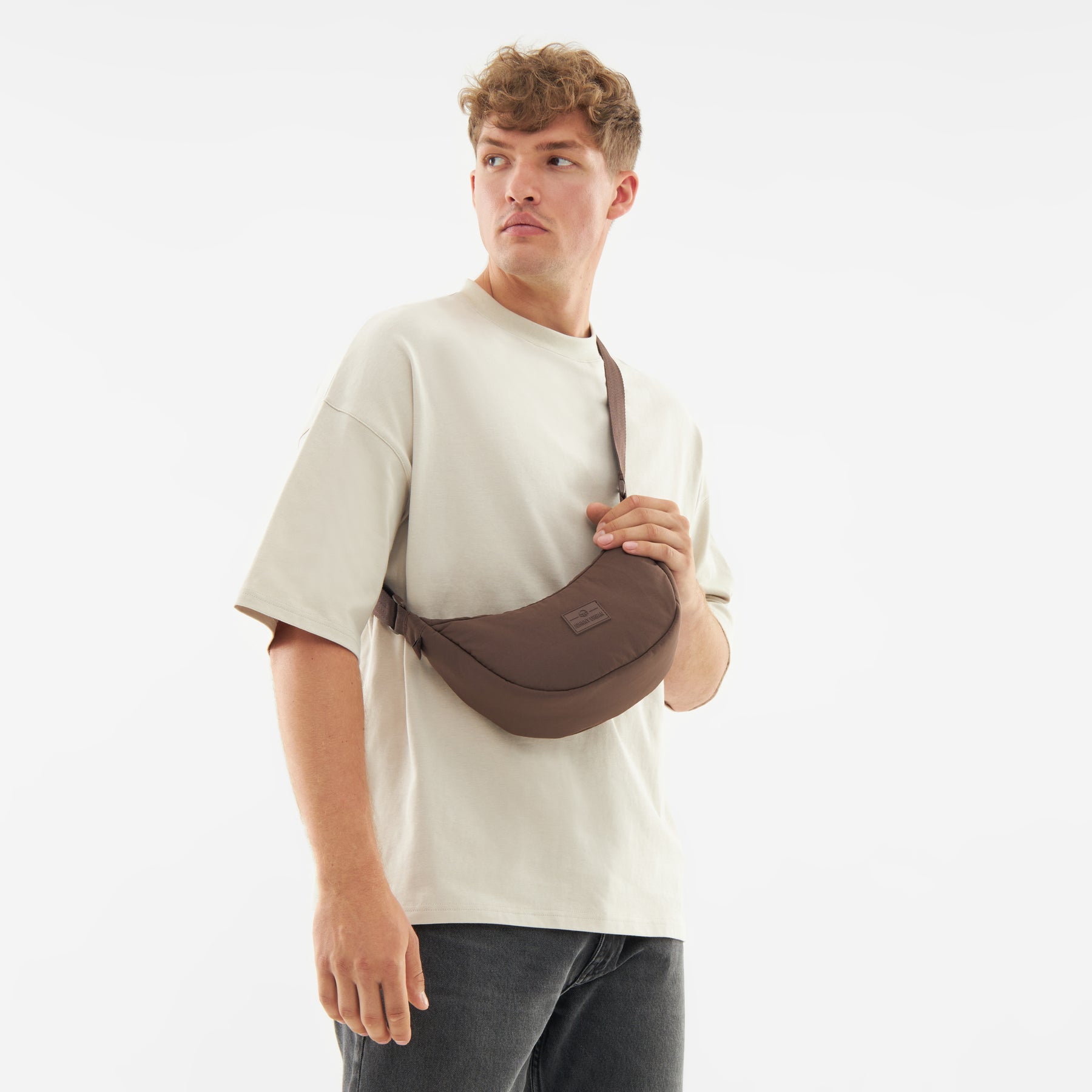 Mann trägt braune Half Moon Bag 'Kaia Small' von Johnny Urban crossbody über ein helles T-Shirt