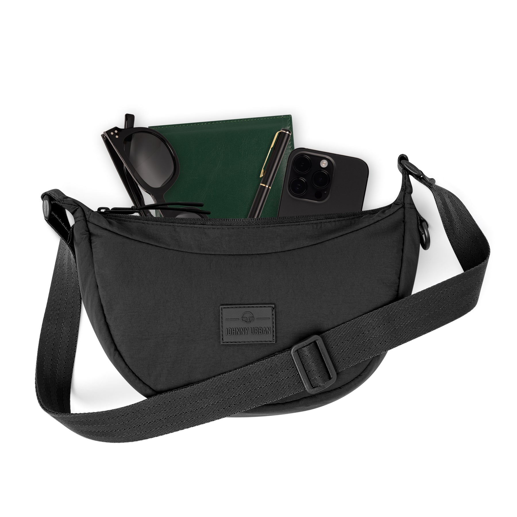 Half Moon Bag 'Kaia Small' von Johnny Urban, schwarze Halbmondtasche mit verstellbarem Schultergurt, geöffnet mit Brille, grünem Notizbuch, Stift und schwarzem Smartphone