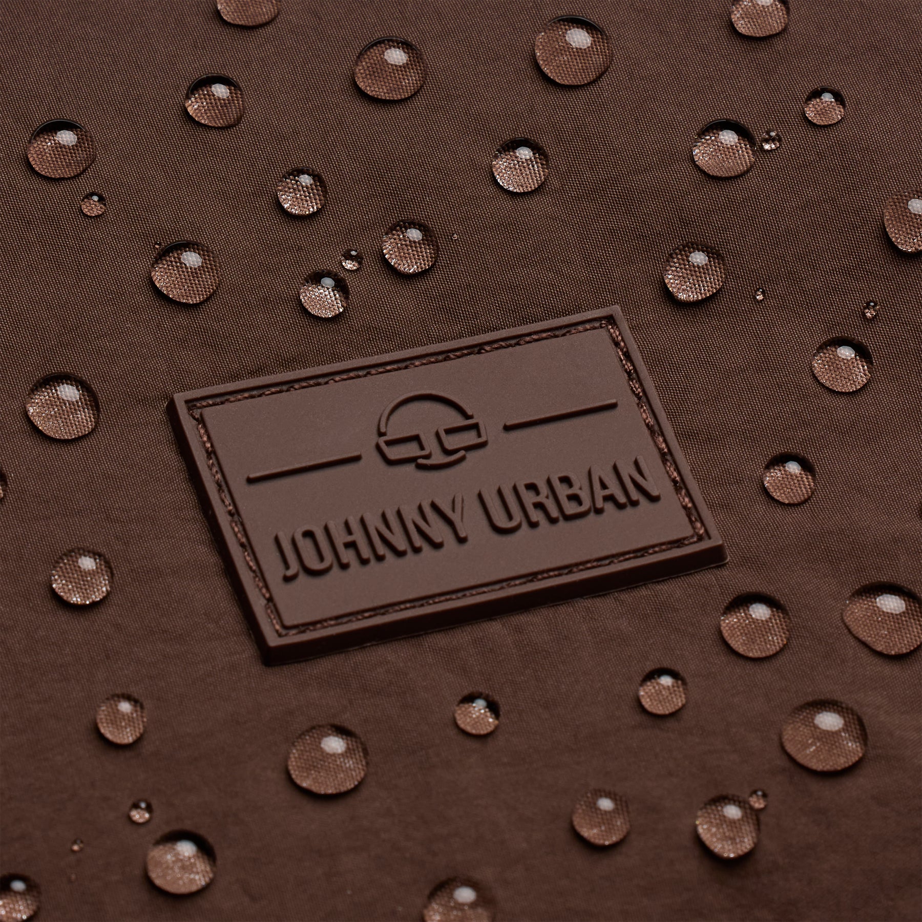 Nahaufnahme des Johnny Urban Logos auf wasserabweisendem braunem Stoff mit Wassertröpfchen