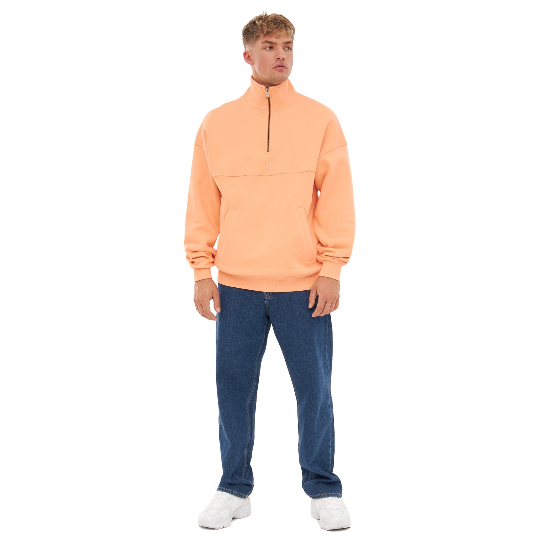 Mann trägt Johnny Urban Half Zip Sweatshirt 'Cooper' in Pfirsichfarbe, kombiniert mit blauer Jeans und weißen Schuhen