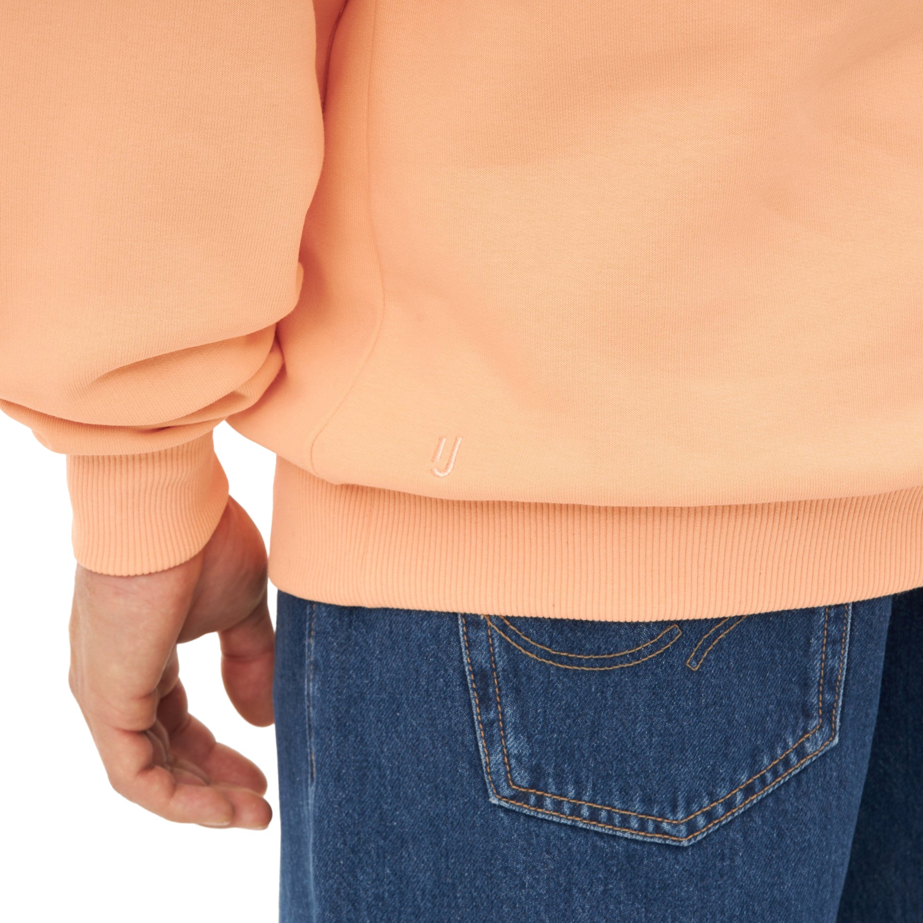 Detailansicht des saumlosen Bündchens eines pfirsichfarbenen Half Zip Sweatshirts 'Cooper' von Johnny Urban über blauen Jeans